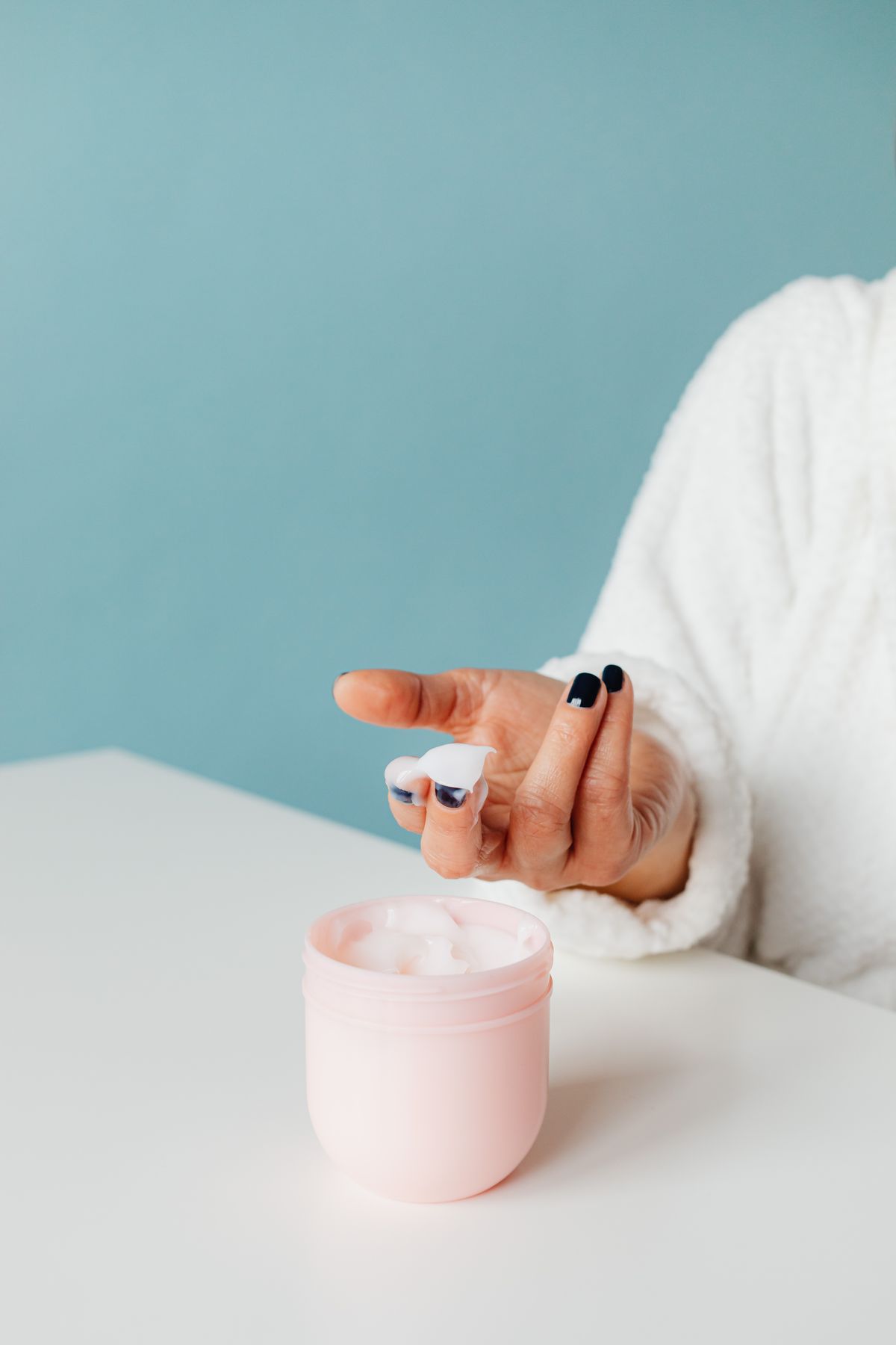A close-up of a hand applying cream from a jar, signifying skincare and hygiene.