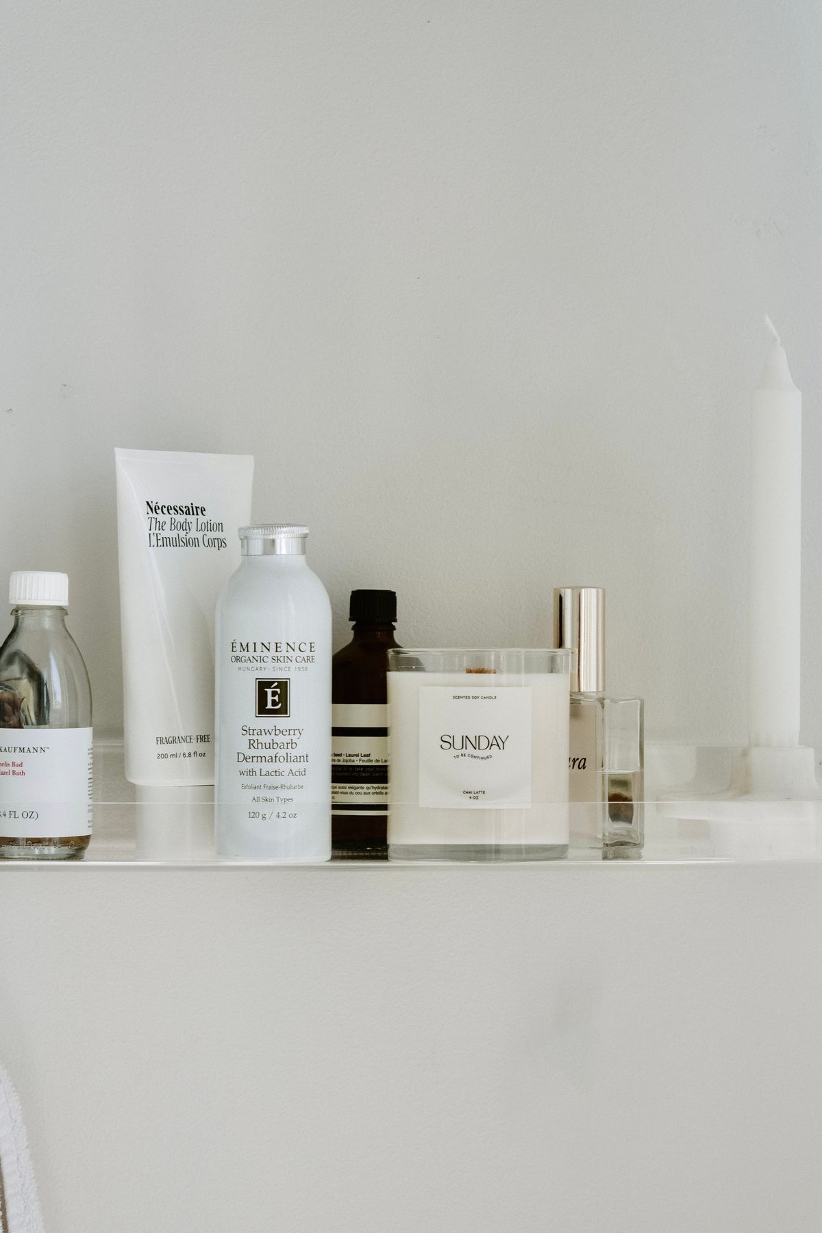 Stylish composition of skincare products and candle on a white shelf, ideal for wellness themes.