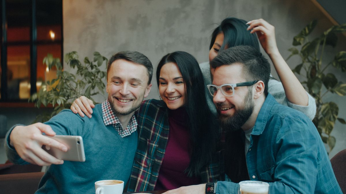 Four friends enjoying a coffee together, smiling and taking a selfie in a cozy cafe setting.