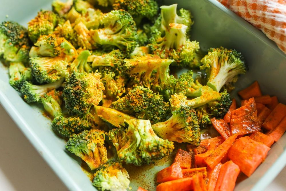 Browned broccoli florets and some carrots in a green baking dish.