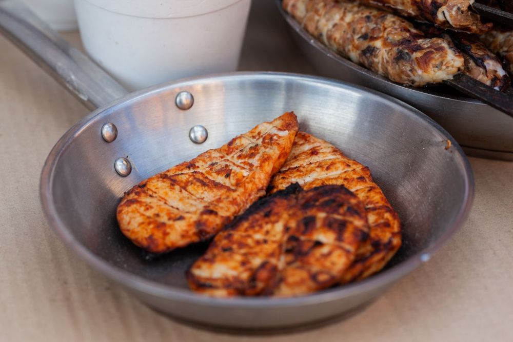 Browned seasoned boneless chicken breasts in a stainless steel pan.