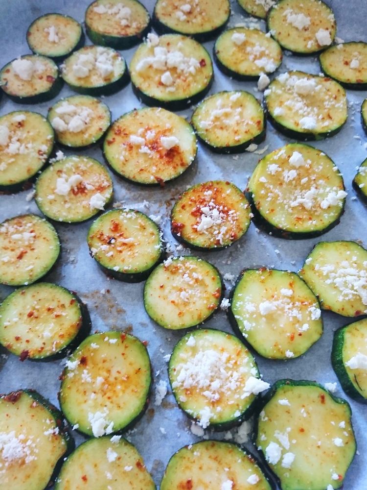 Browned zucchini rounds on a baking tray sprinkled with white cheese.