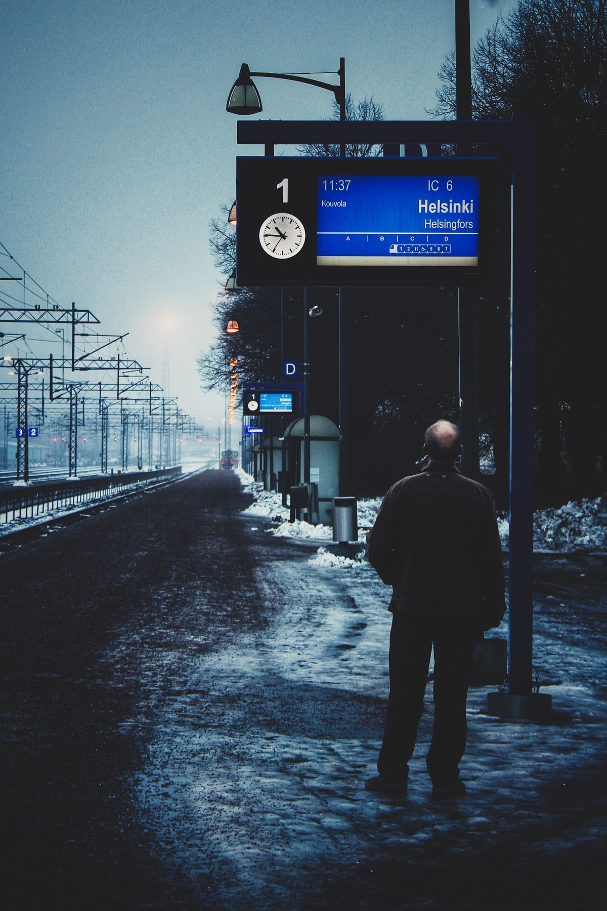Man stands in snow at Lappeenranta station, viewing Helsinki train schedule.