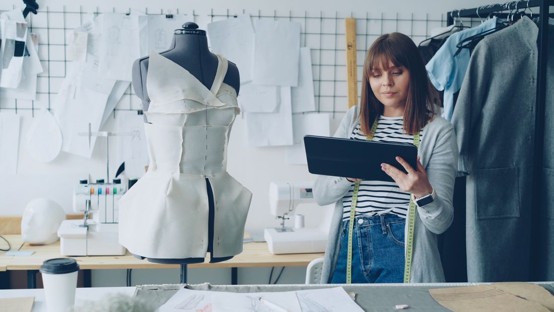 A fashion designer with a tablet and dress form in a studio.