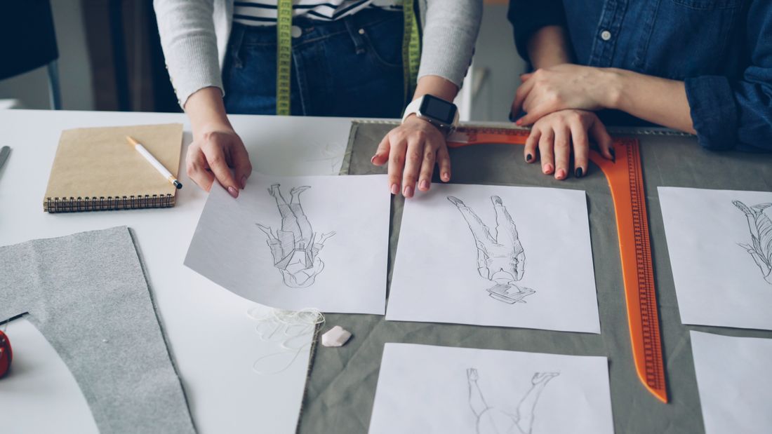 Two fashion designers discussing sketches and fabric samples at a desk.
