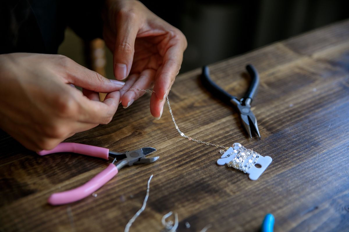 Close-up of hands crafting jewelry with pliers and wire on a wooden table.