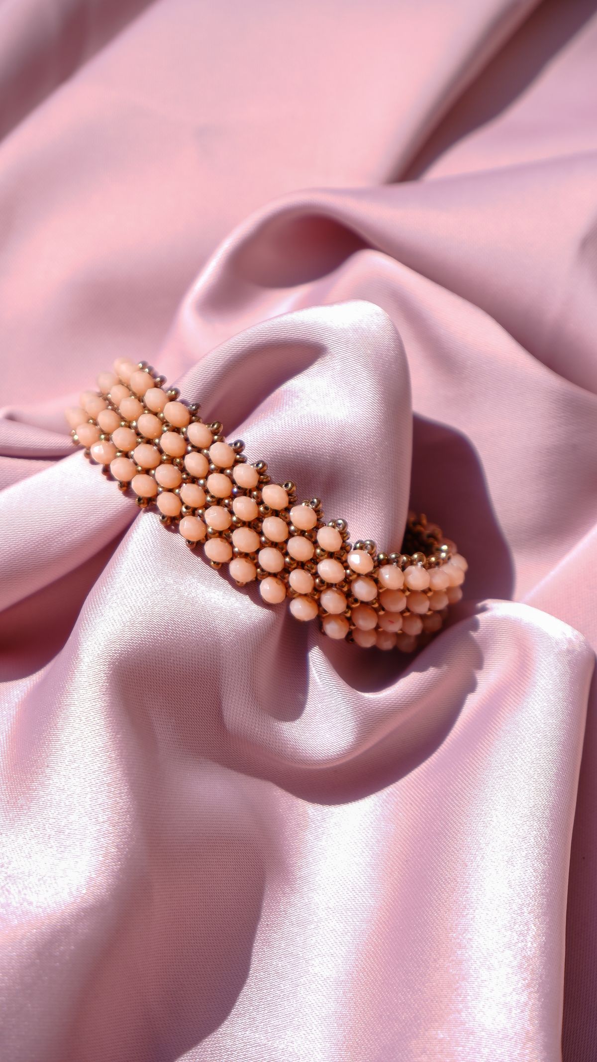 A close-up of a chic beaded bracelet elegantly displayed on pink satin fabric, showcasing luxury and style.