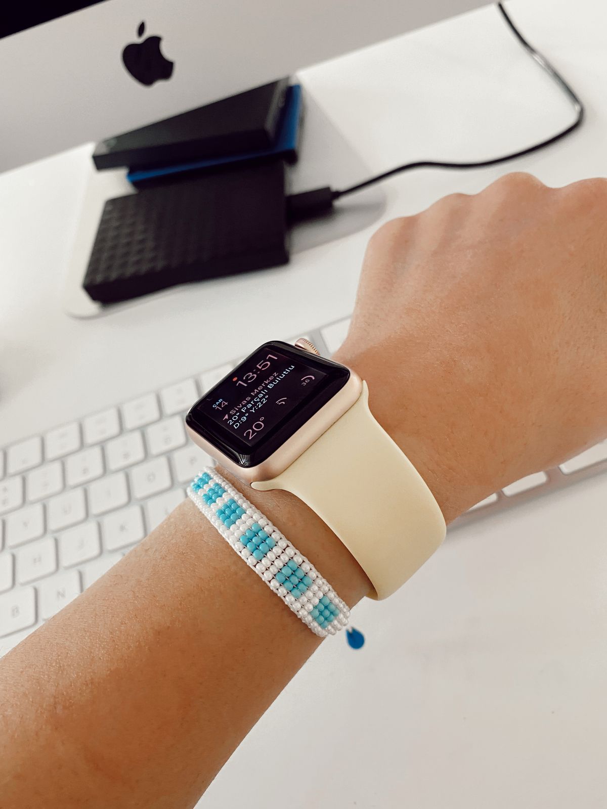 A close-up view of a person's wrist wearing a smartwatch and a beaded bracelet in an office setting.