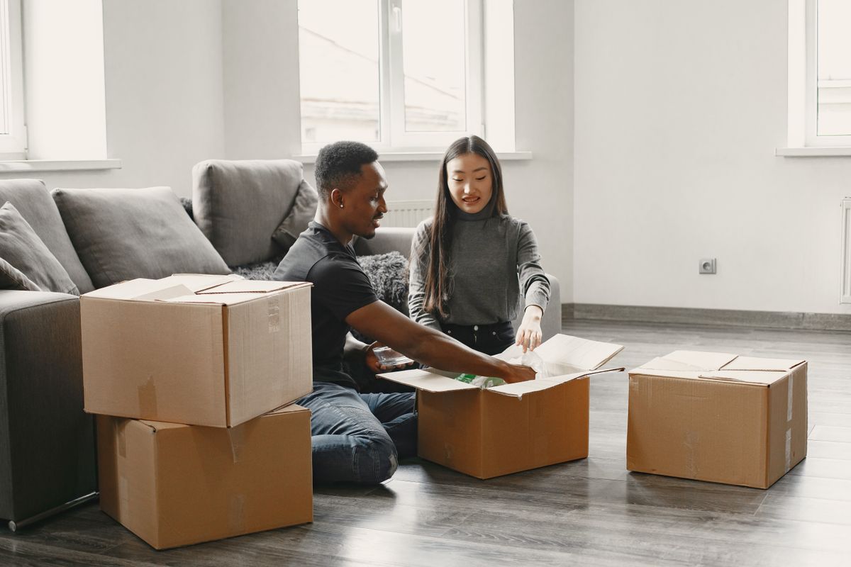 Happy couple unpacking moving boxes in their new apartment living room.