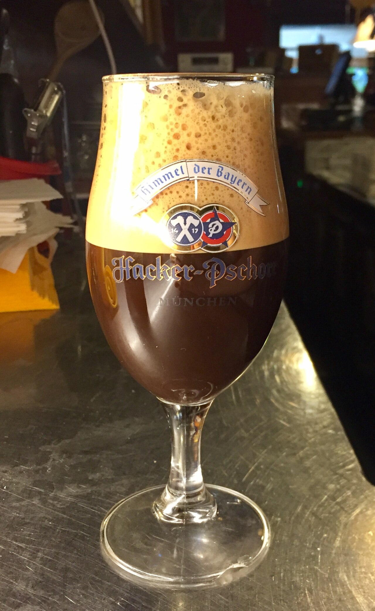 Dark shakerato with a thick tan foam head in a rounded stemmed glass.