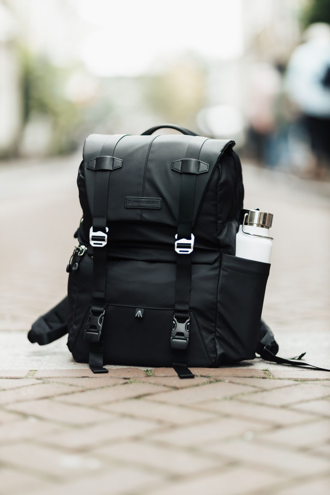 A black backpack with a bottle in its side pocket.