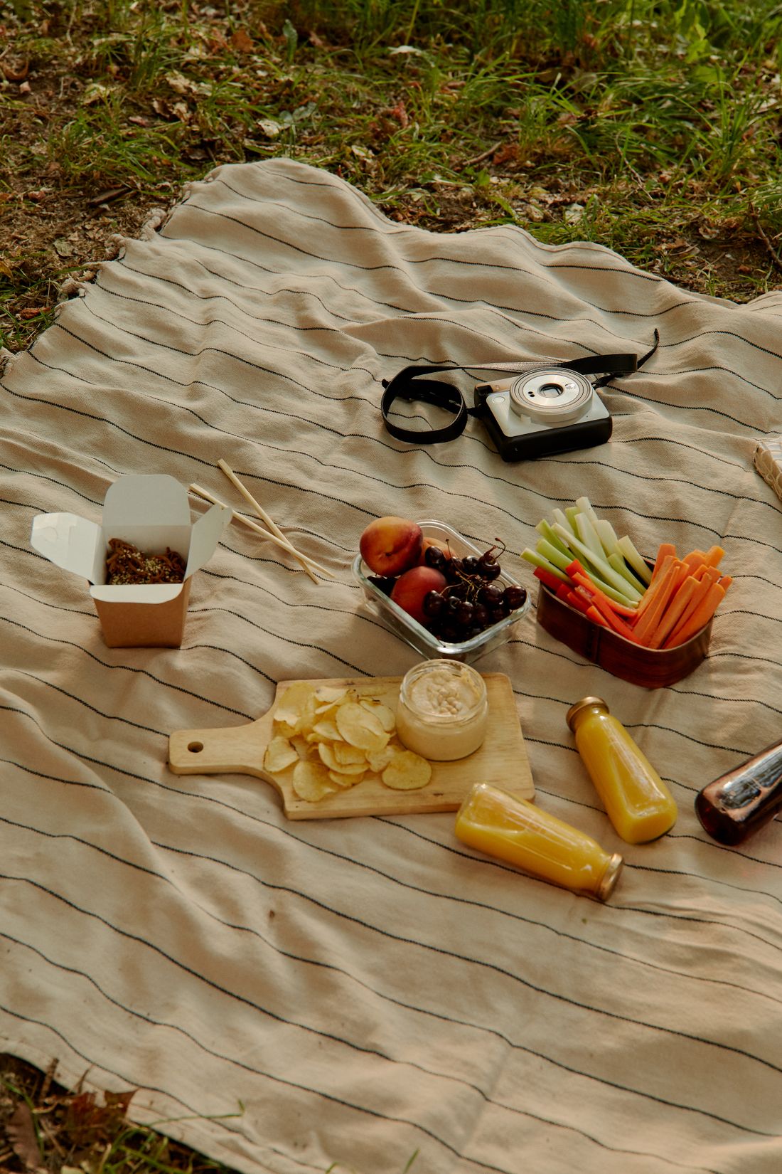 Snacks and drinks arranged on a striped picnic blanket.