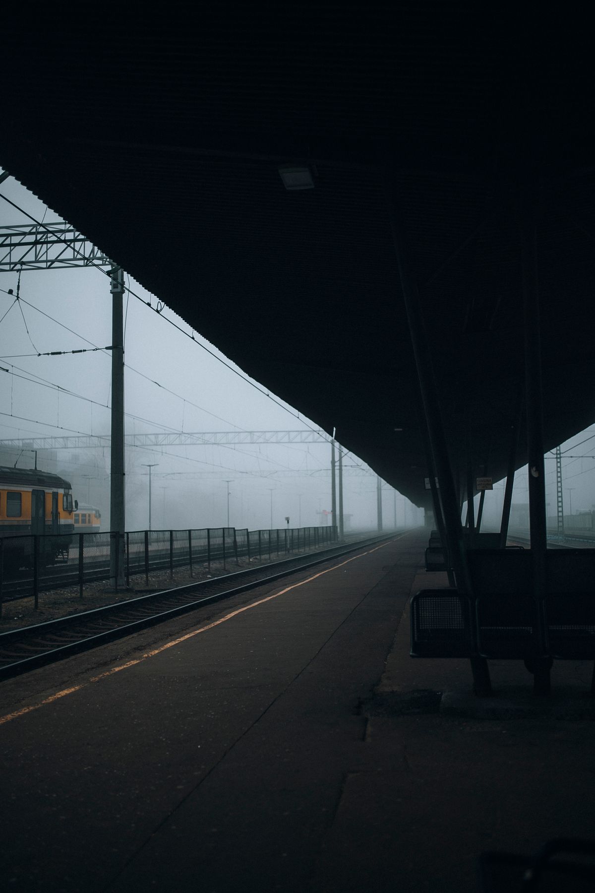 Misty railway platform with empty benches and train under foggy sky, evoking an atmospheric mood.