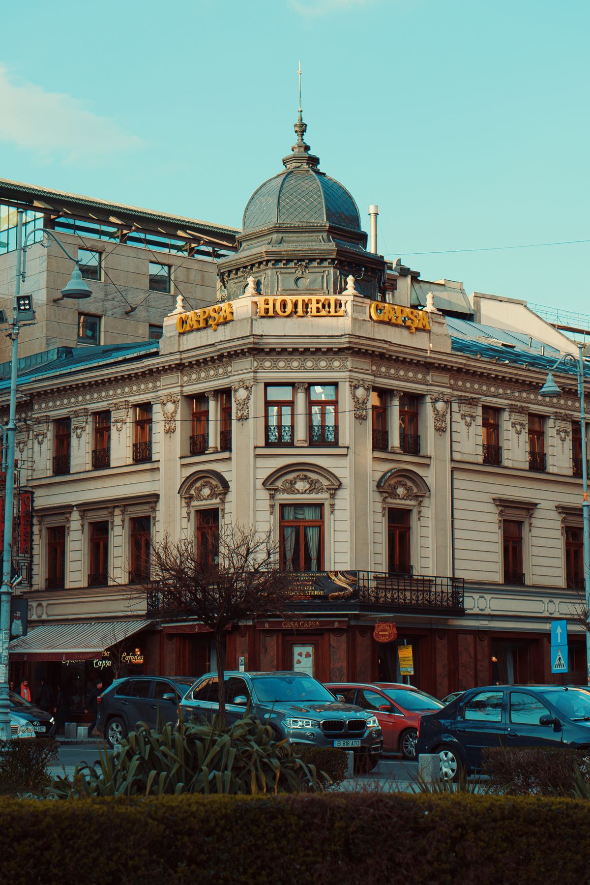 Elegant historic hotel facade on a city corner with parked cars, showcasing classic European architecture.