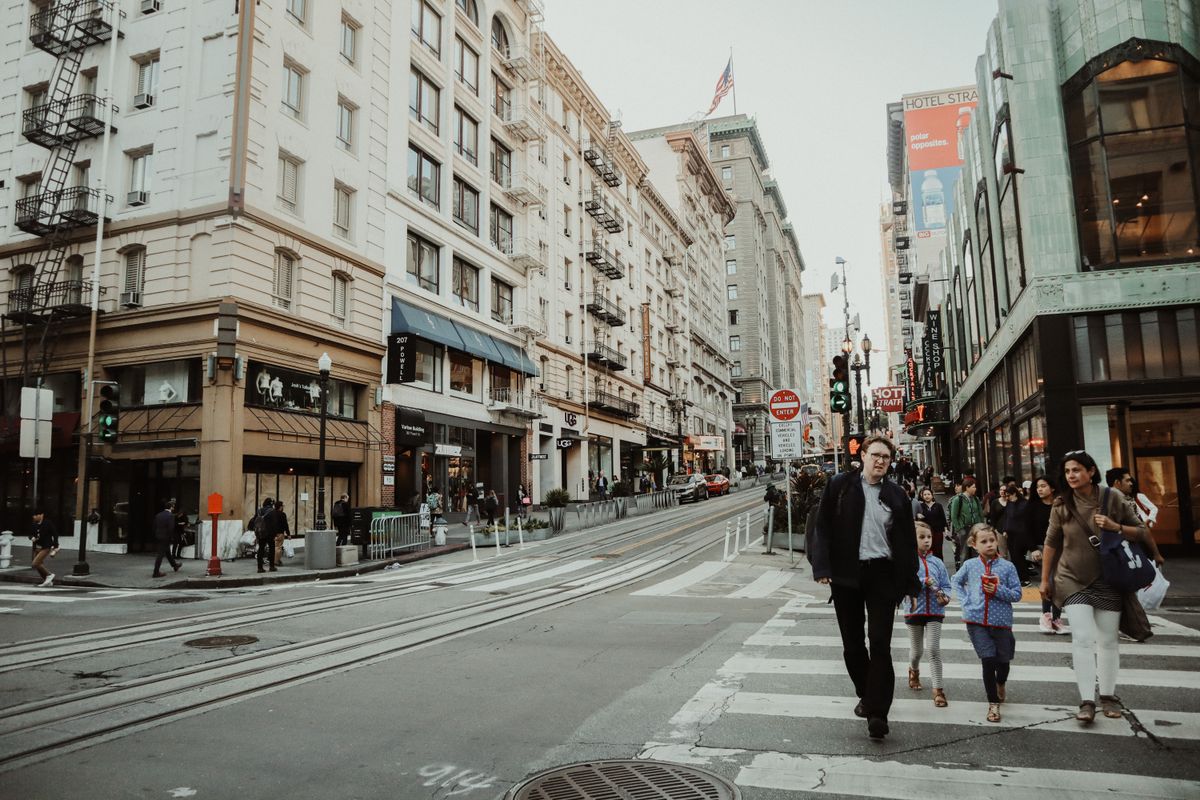 Vibrant city street with people crossing at a busy intersection on a lively day.