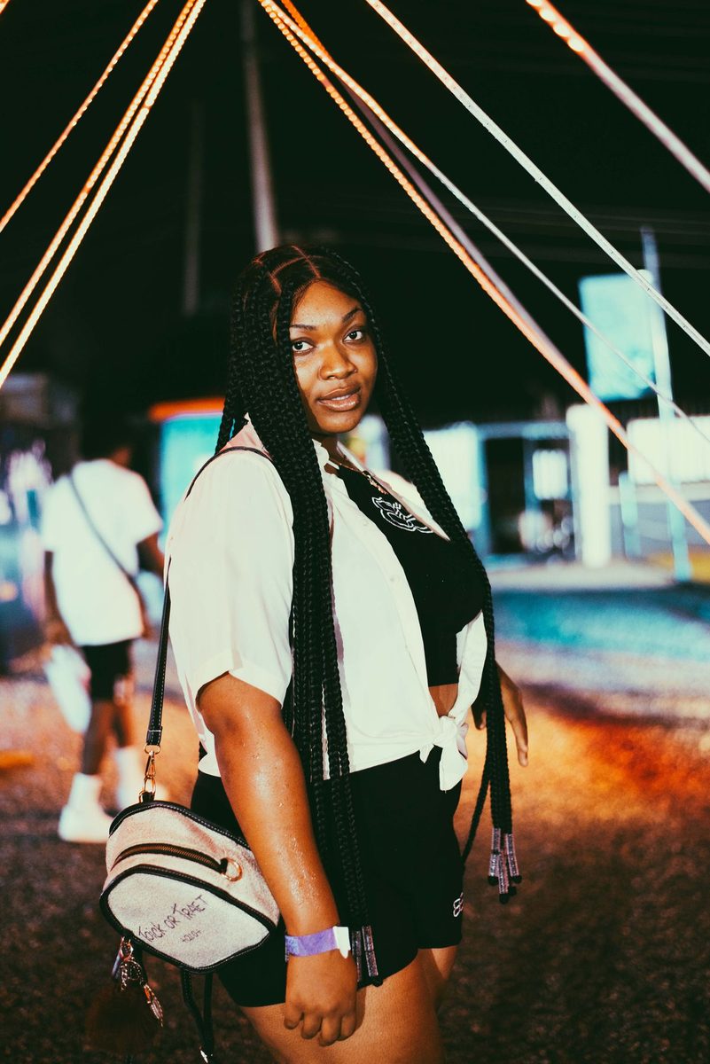 Woman with braided hair, a white overshirt and a shoulder bag at a festival.