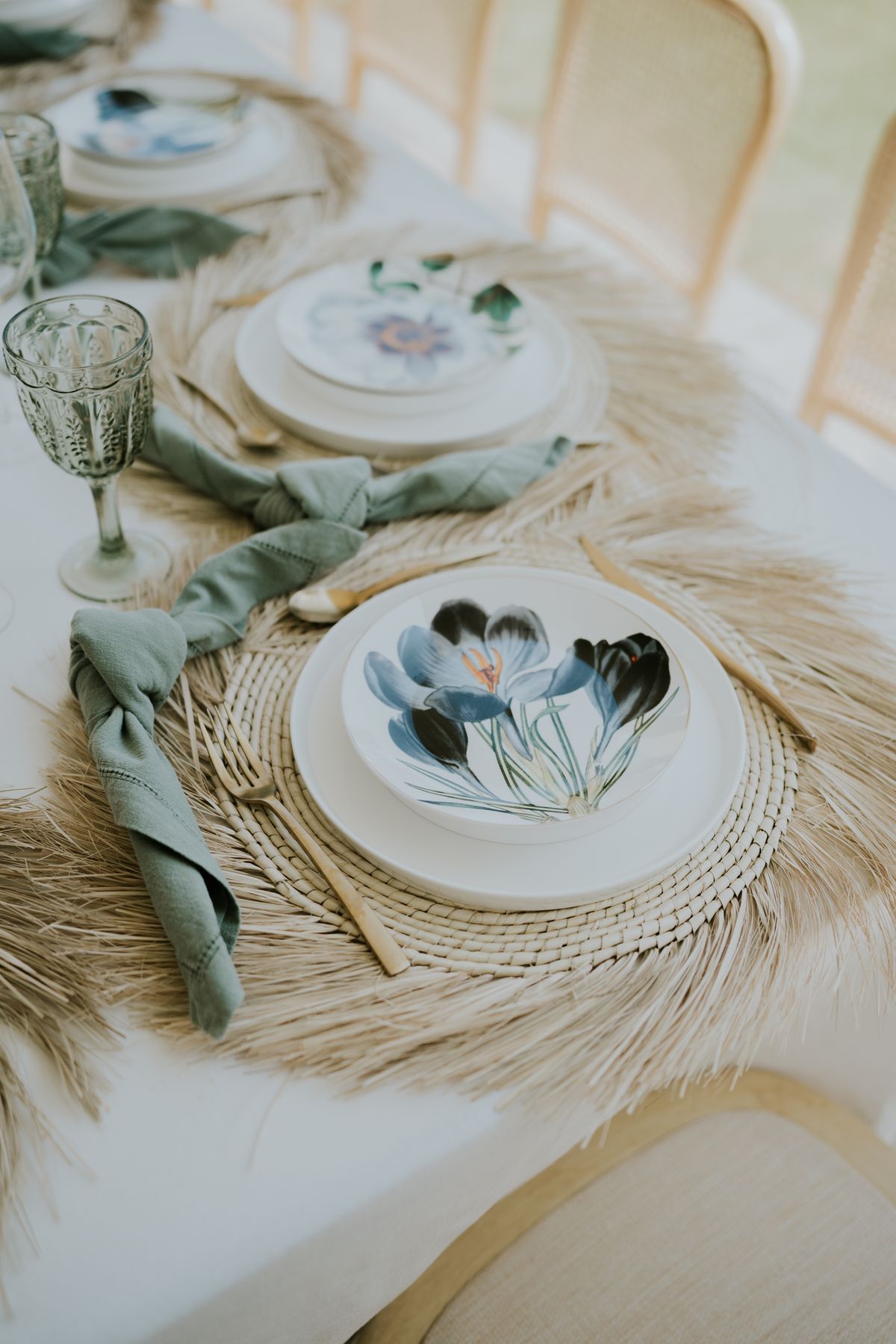 Stylish dining setup featuring floral plates, green napkins, and wicker placemats for a modern, earthy vibe.