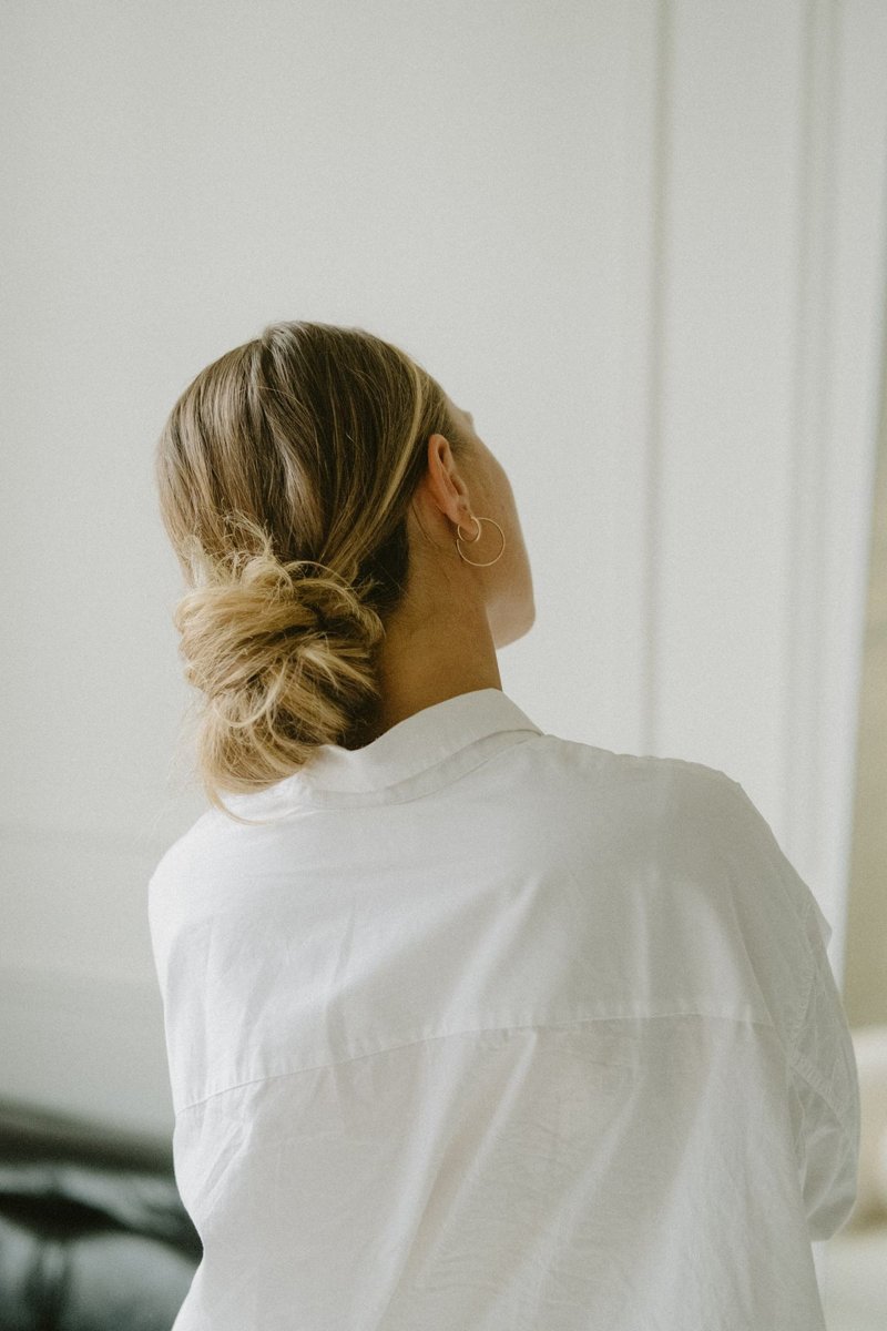 Rear view of a woman wearing a low bun with a white shirt.