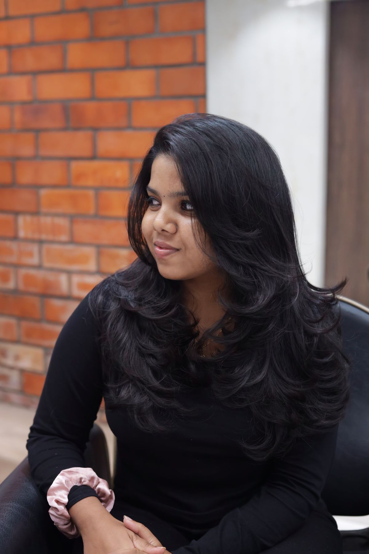 Stylish portrait of a woman with long black hair in a black outfit sitting indoors.