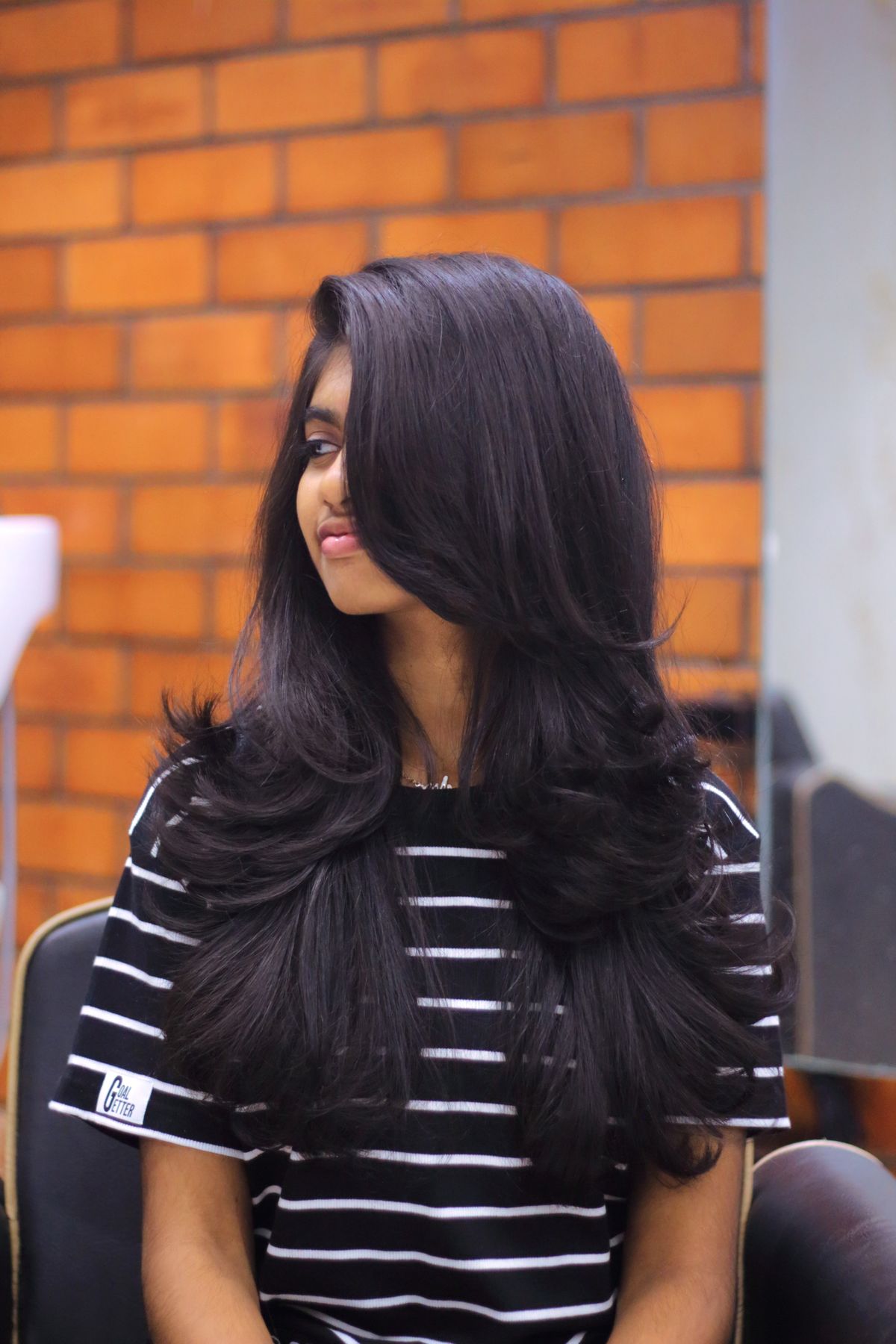 Portrait of a woman with long layered hair sitting indoors at a hair salon.