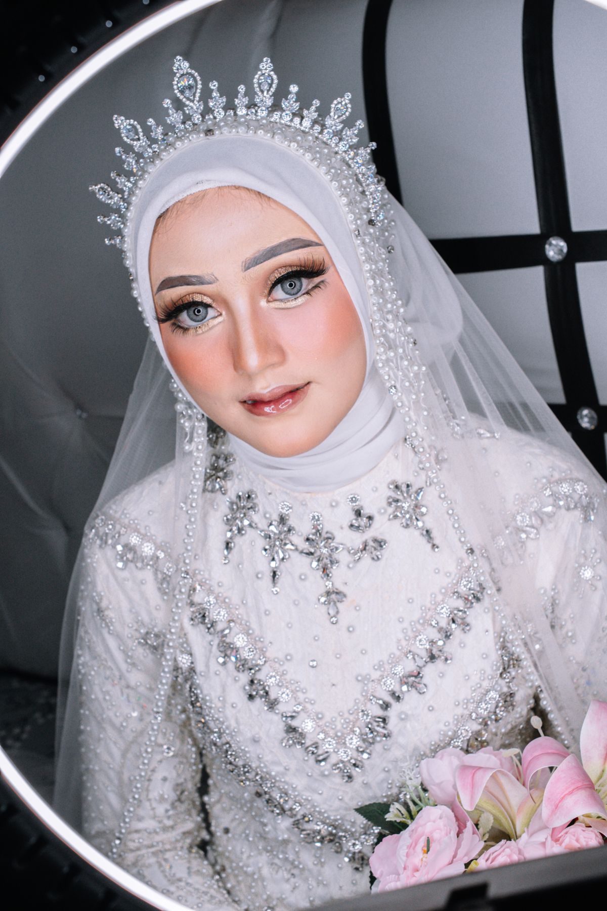 Beautiful Muslim bride in sparkling gown, holding pink bouquet. Captures elegance and joy.