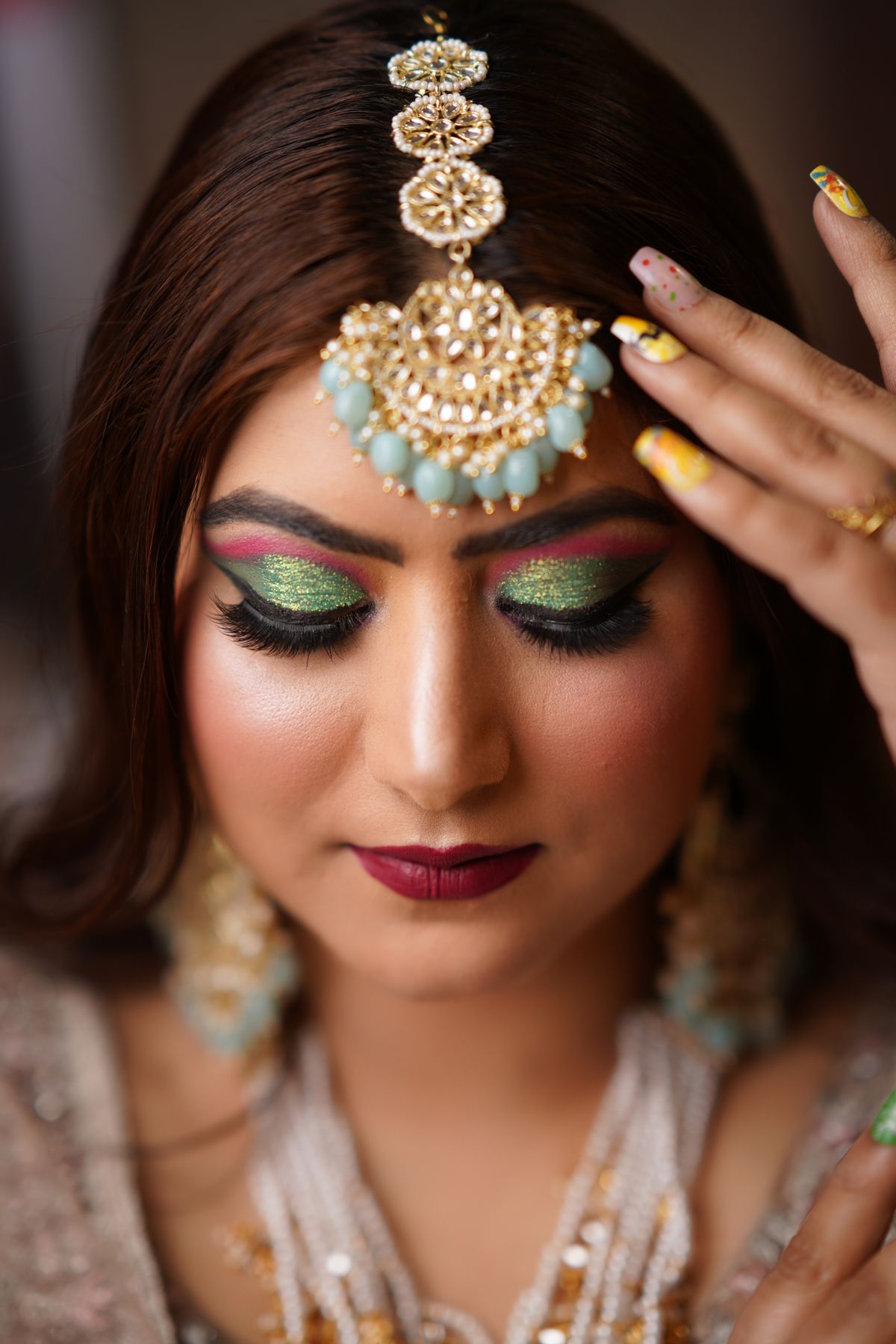 Close-up of an Indian bride wearing a stunning maang tikka and glamorous makeup.