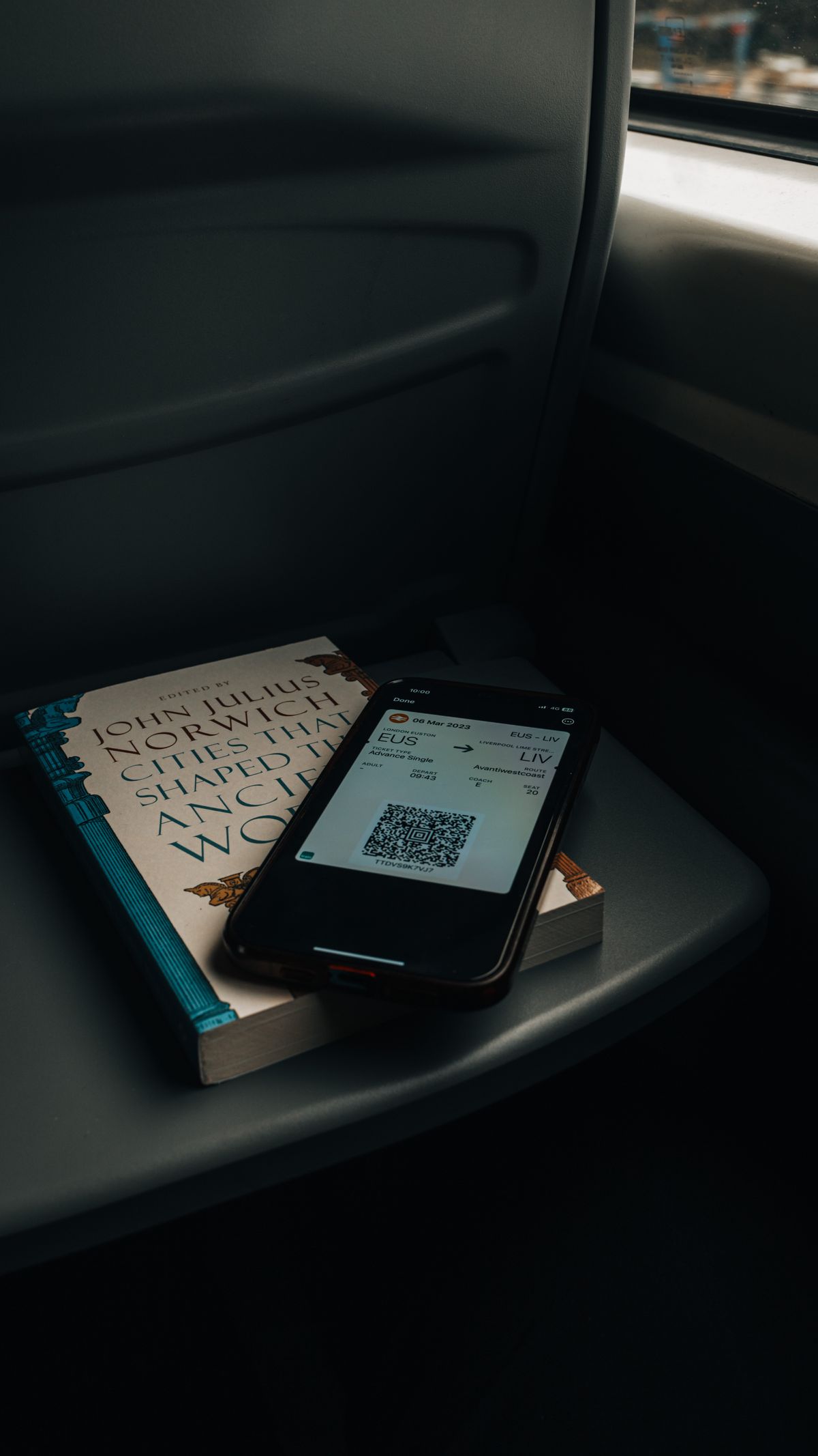 A mobile phone displaying a QR code placed on a book, captured in a dimly lit environment.