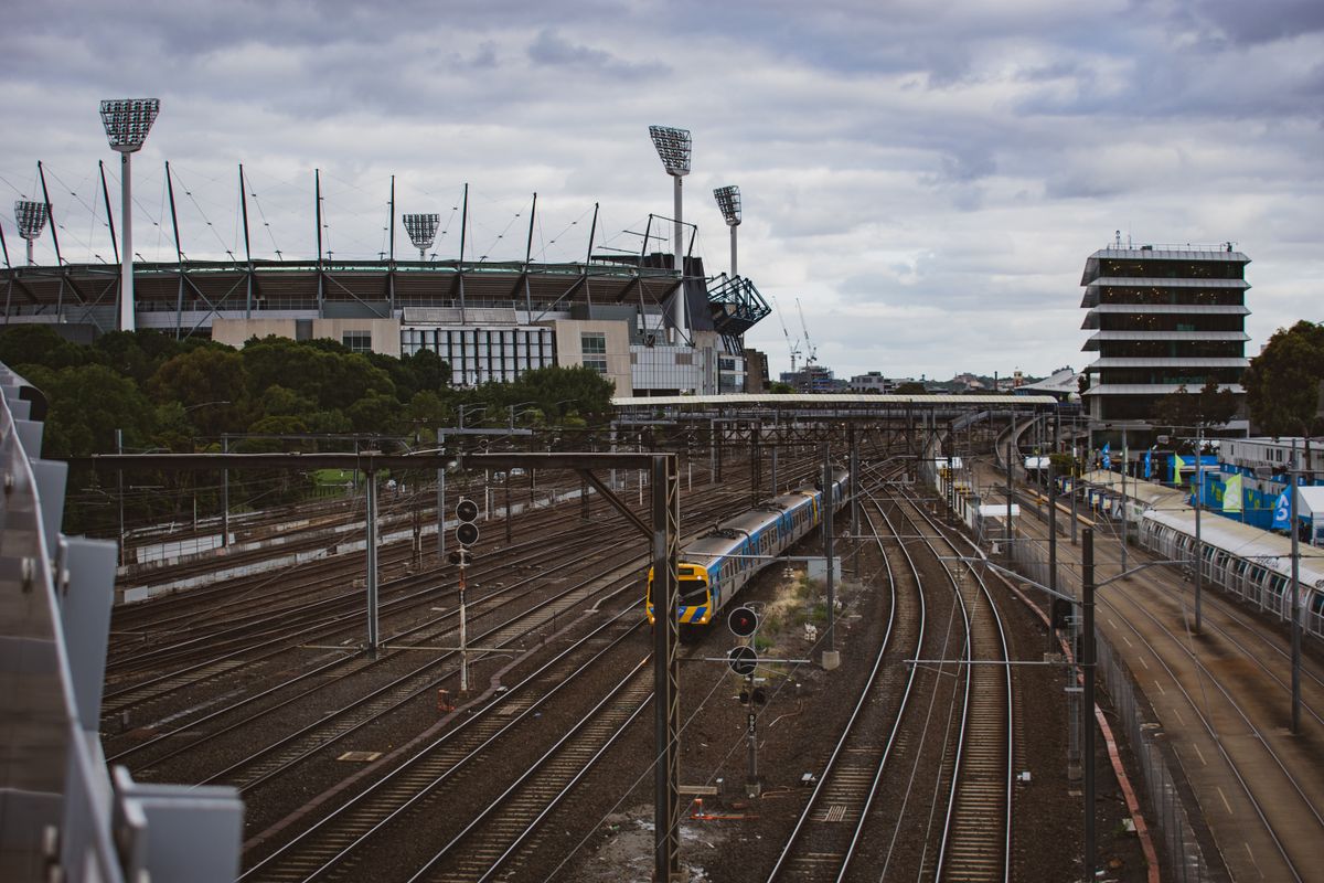 A train travels on tracks near a stadium in Melbourne, showcasing urban transportation and iconic landmarks.