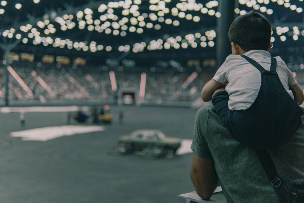 Father and son from behind in a stadium watching an indoor motorsport event.