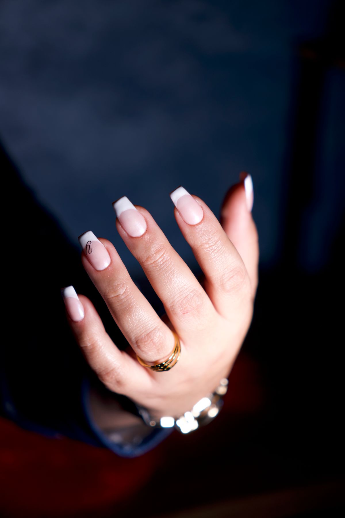 Graceful, manicured hand with elegant jewelry, showcasing stylish nails against a dark backdrop.