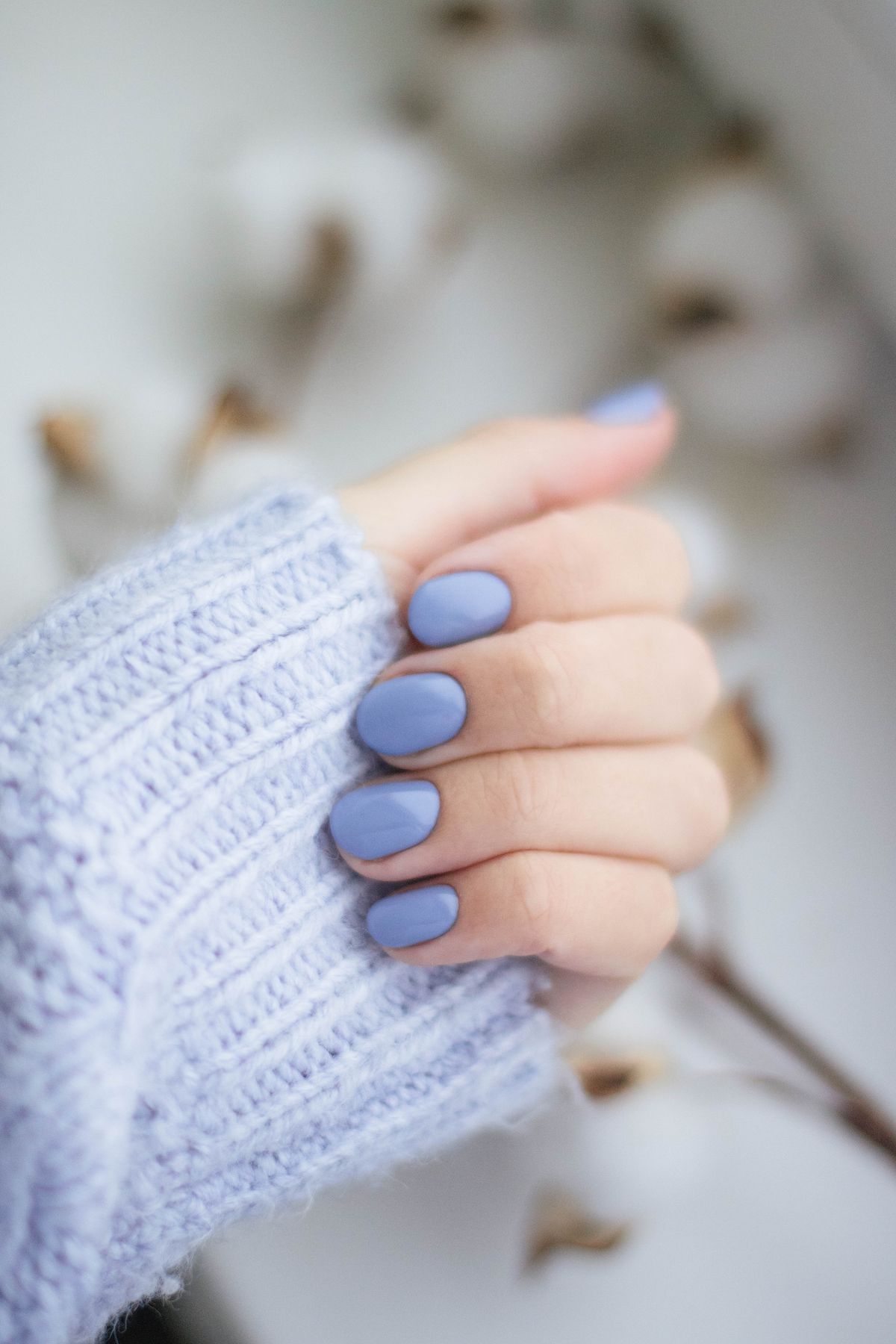 A close-up of a woman's hand with purple manicured nails and knitwear, showcasing trendy fashion.