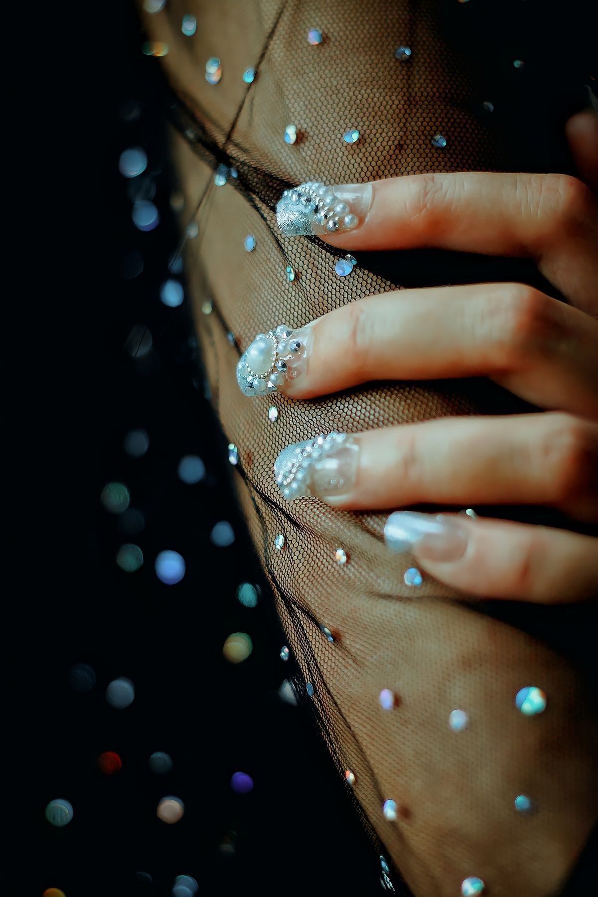 Close-up of a stylish hand with dazzling manicured nails on mesh fabric, adorned with sparkles.