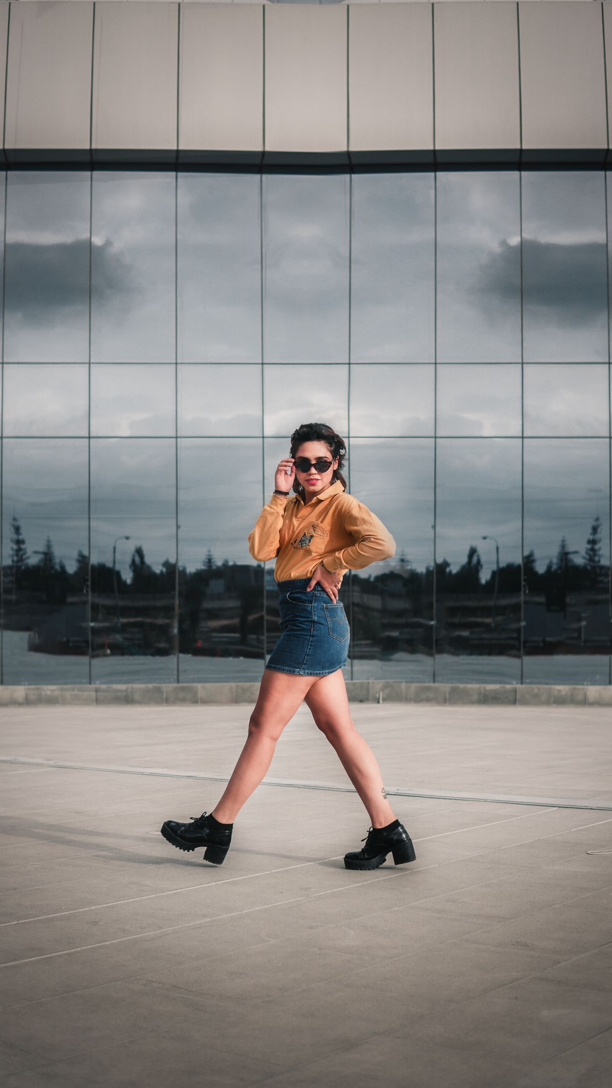 Stylish woman in denim and boots posing by a glass building in Peru.