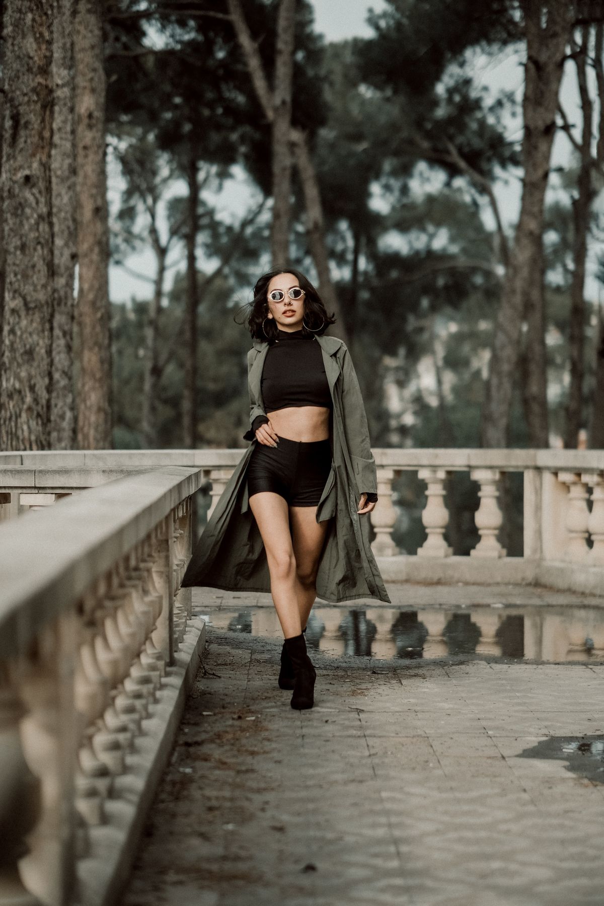Confident woman in sunglasses and long coat walking outdoors, exuding style and grace.