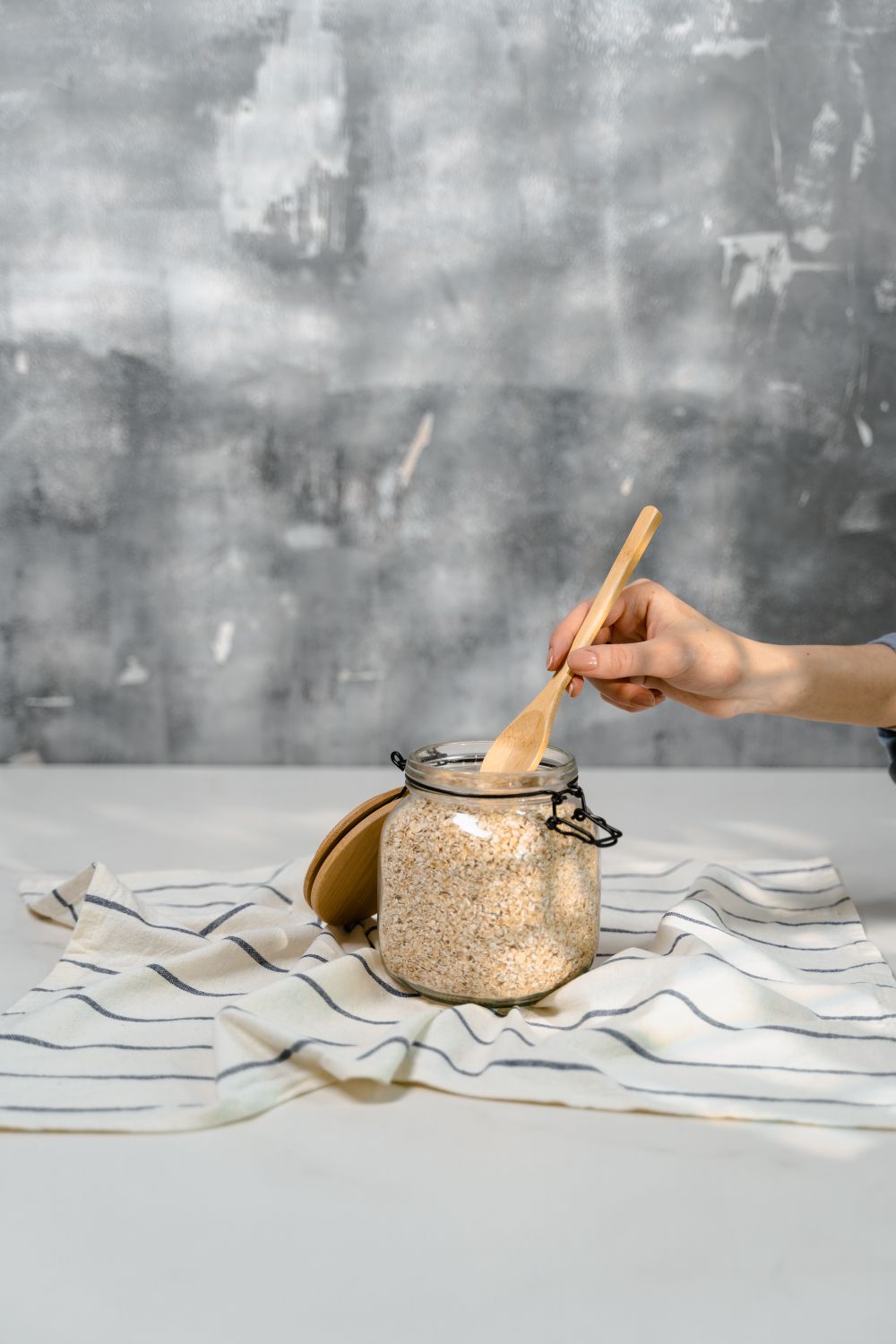 Oats stirred in a glass jar on a striped cloth.