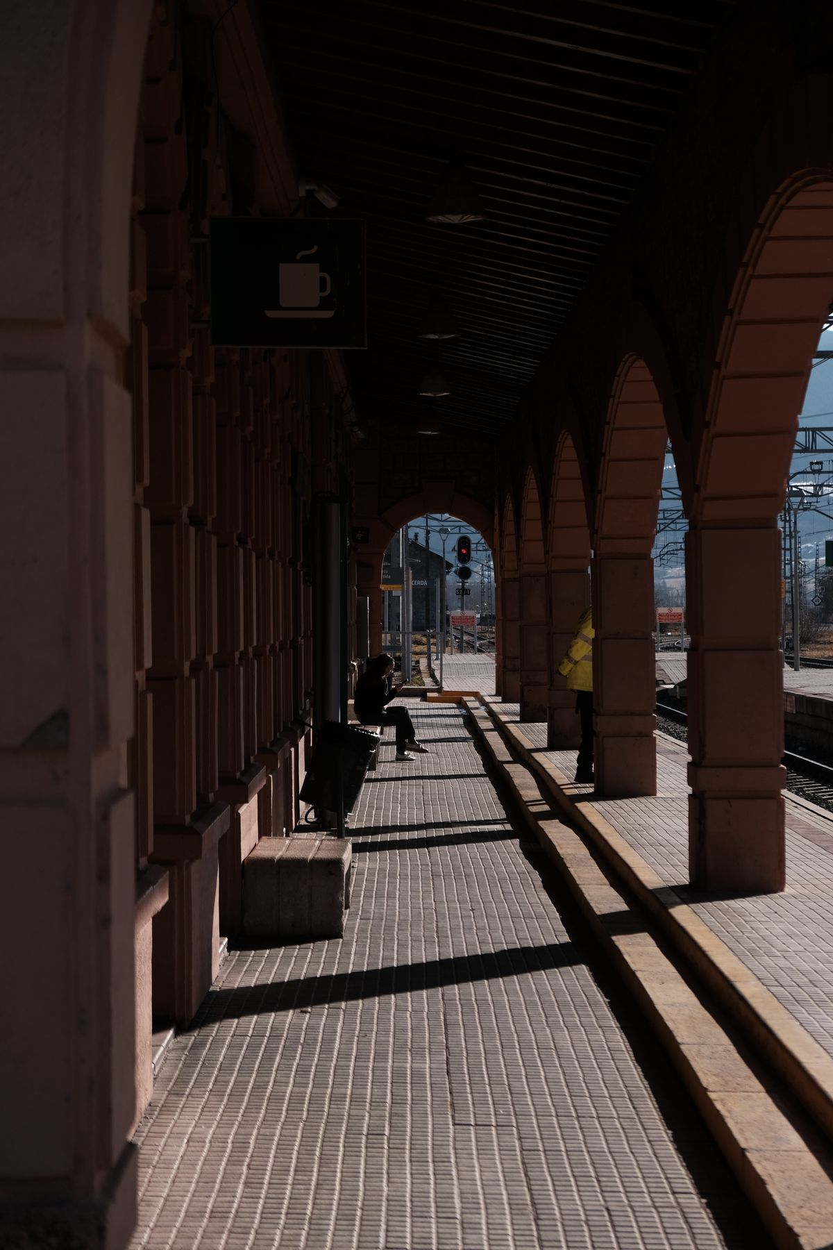 A sunlit hallway with arches at a train station, casting dramatic shadows.