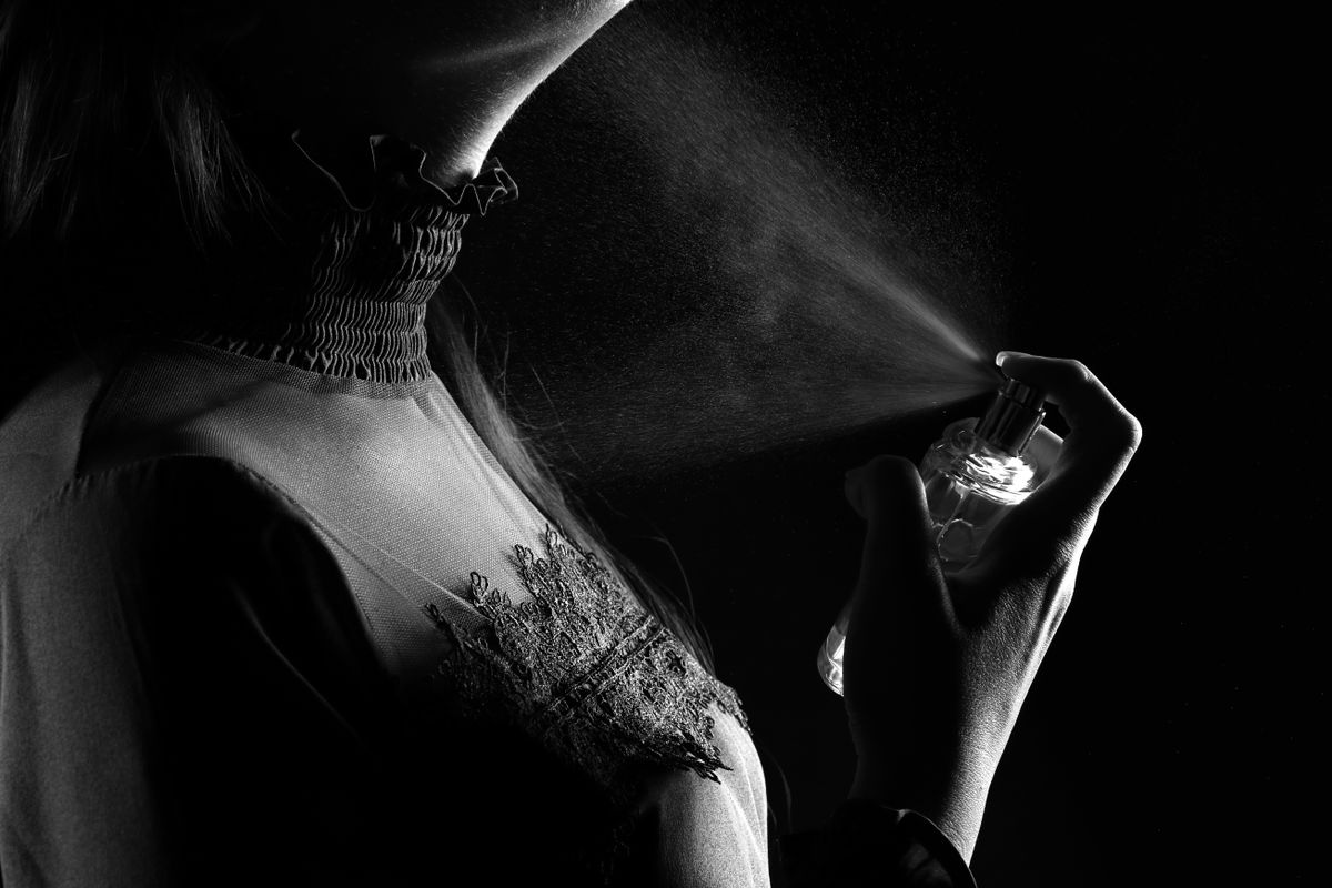 A stylish woman sprays perfume, captured in a dramatic black and white studio shot.