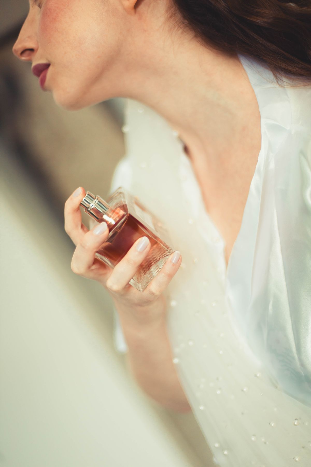A bride elegantly applies perfume, showcasing delicate bridal details in a serene setting.