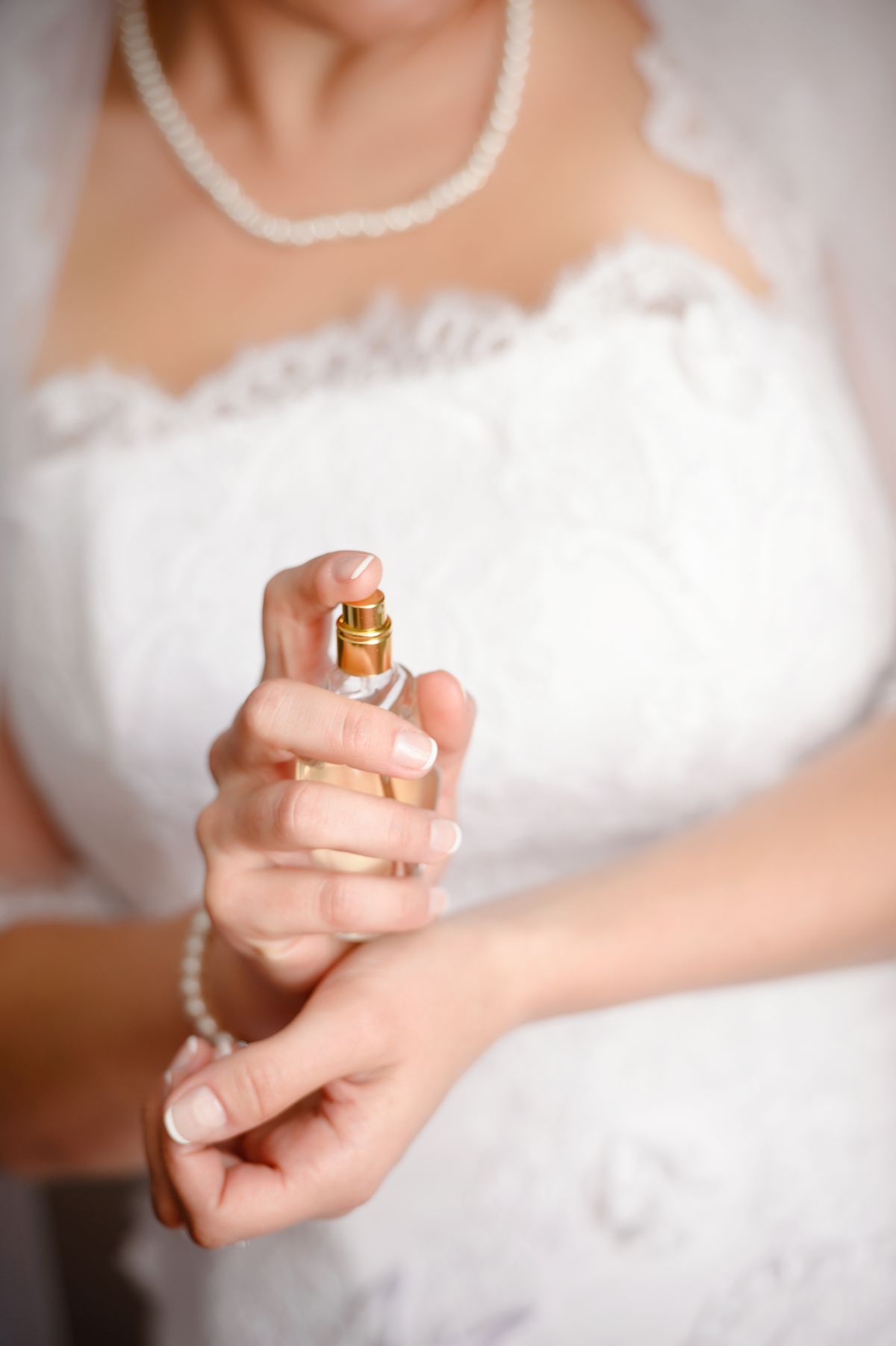 Bride in white lace dress applying perfume on wrists, preparing for her wedding day.