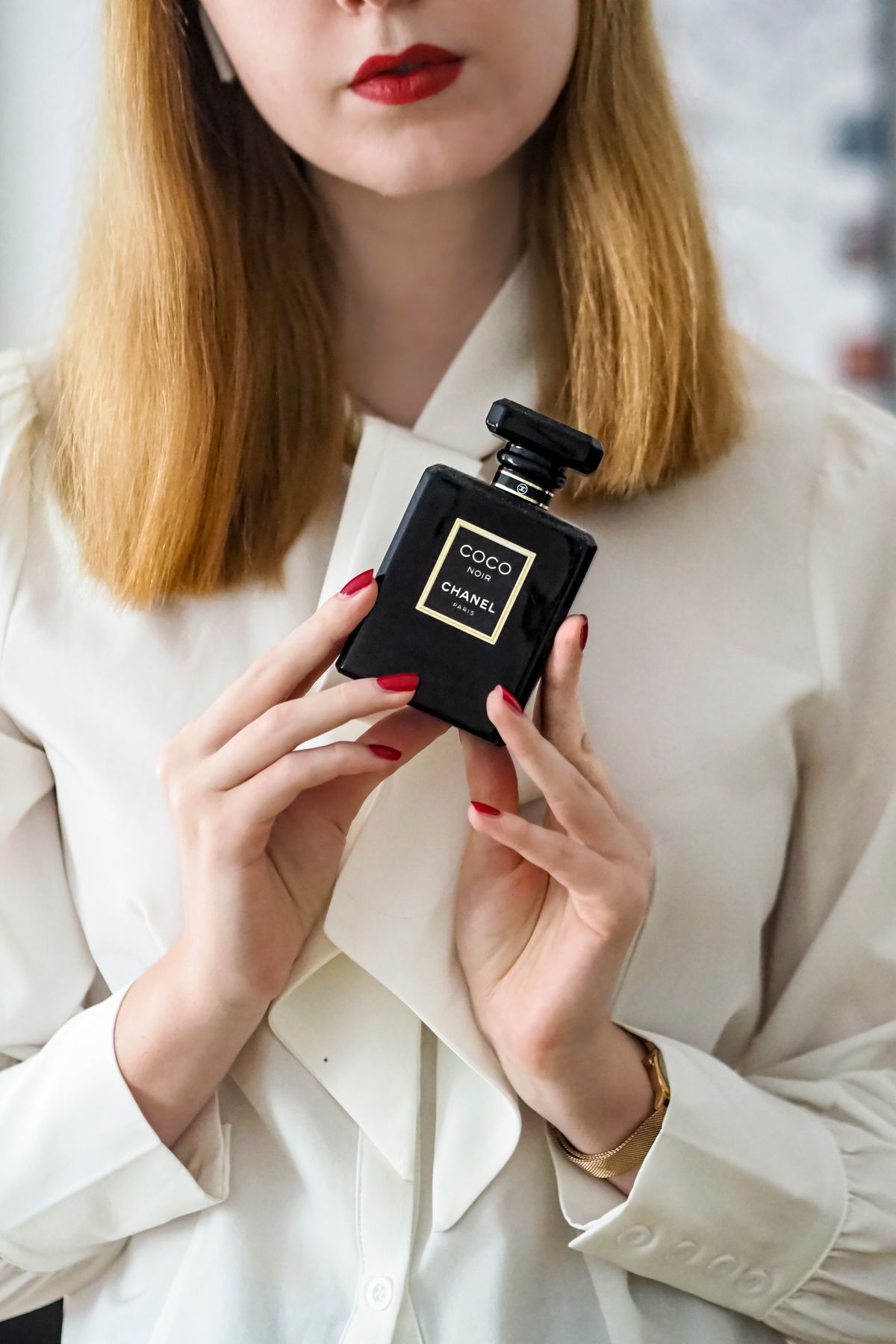 Stylish woman in white blouse holding luxury perfume indoors.