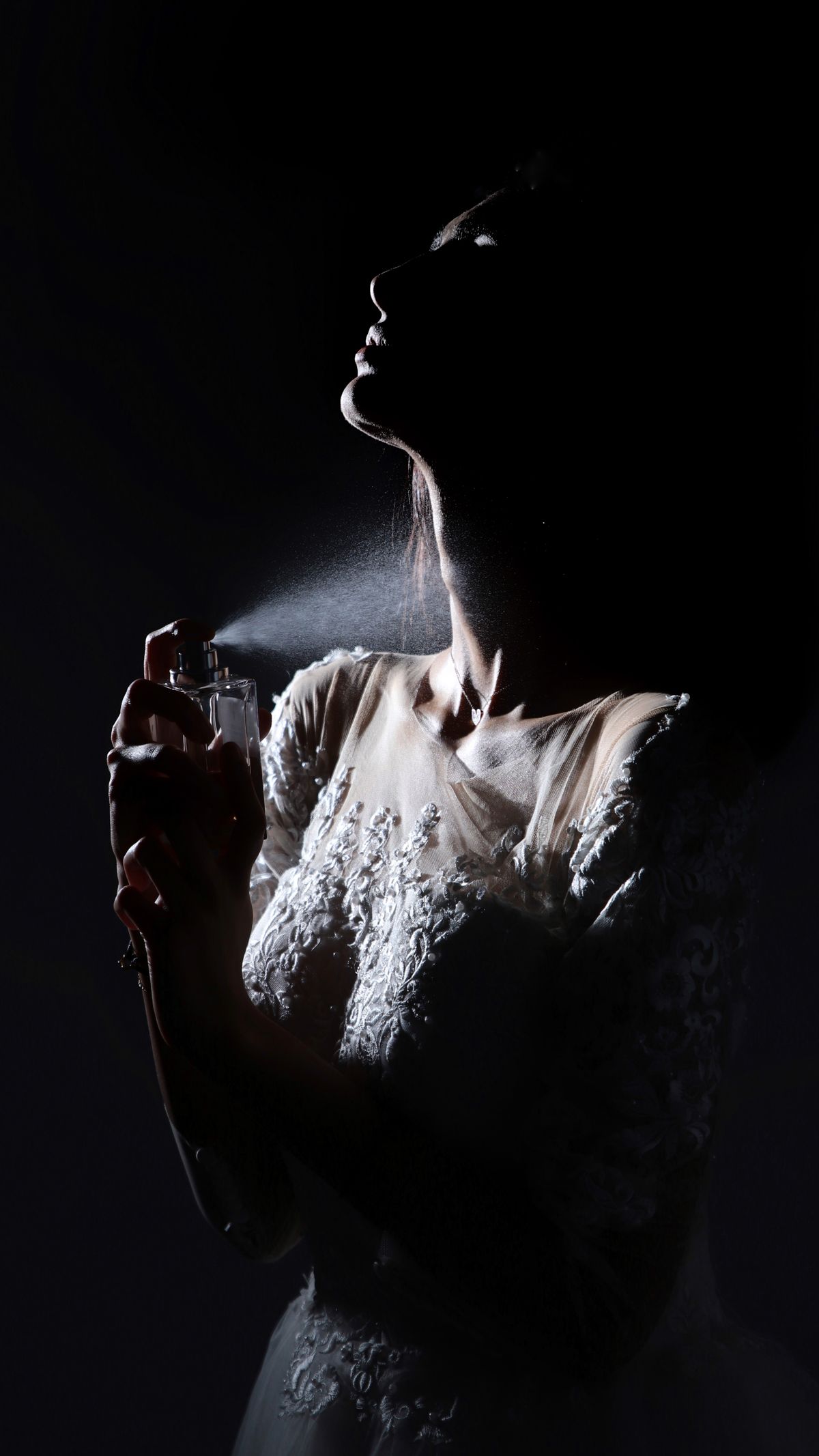 Artistic black and white portrait of a bride in a shadowy ambiance applying perfume before her wedding.