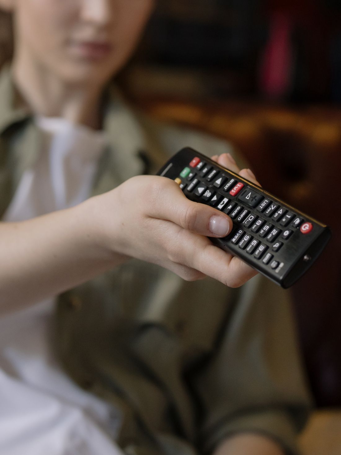 A person holding a television remote in a relaxed home setting.