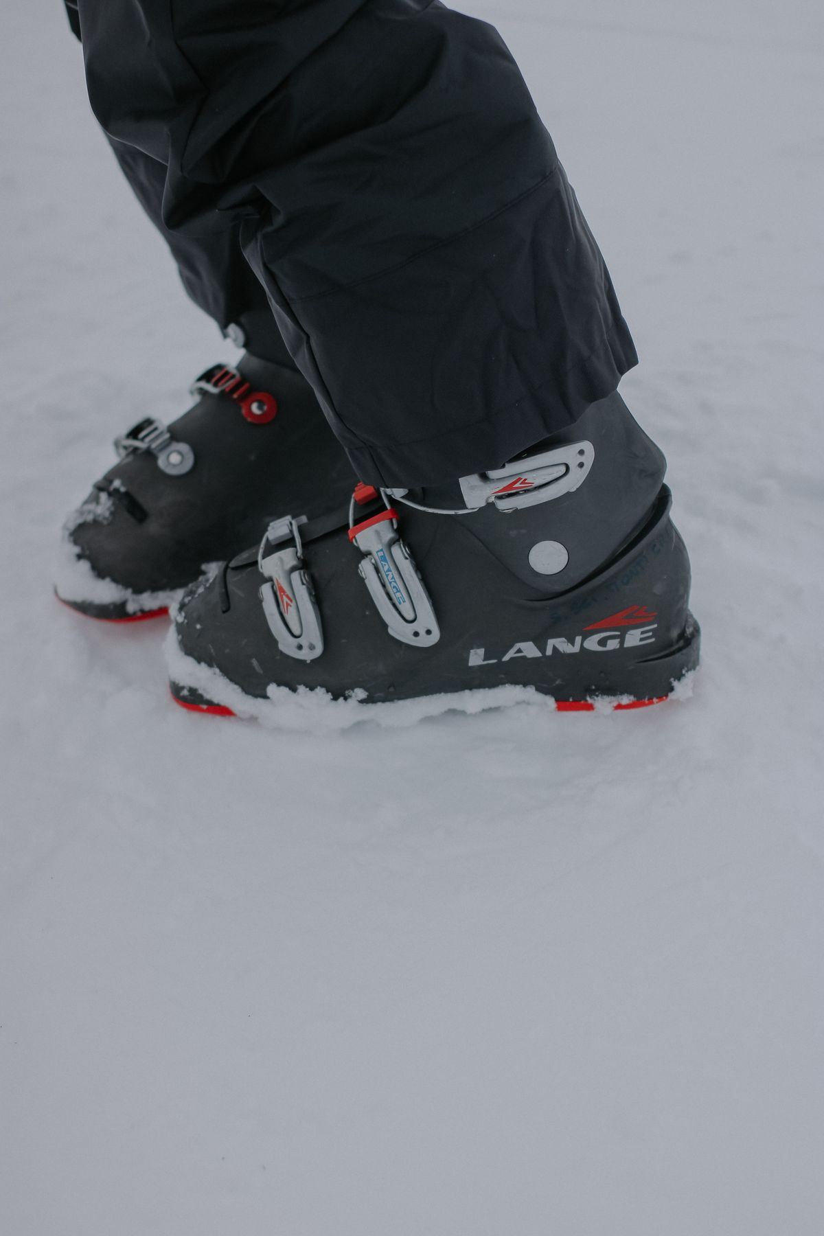 Detailed view of ski boots worn by a skier standing in snow, highlighting winter sports equipment.