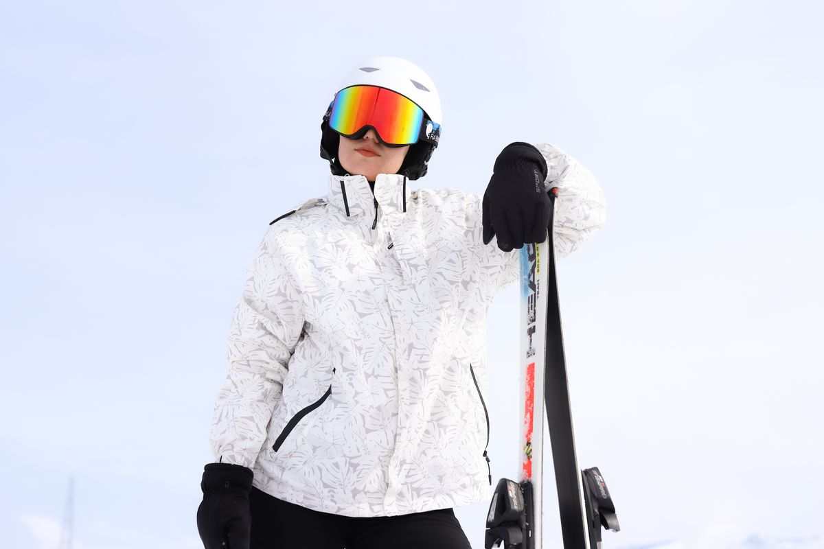 Adult skier poses confidently with skis on a snowy mountain in bright gear.