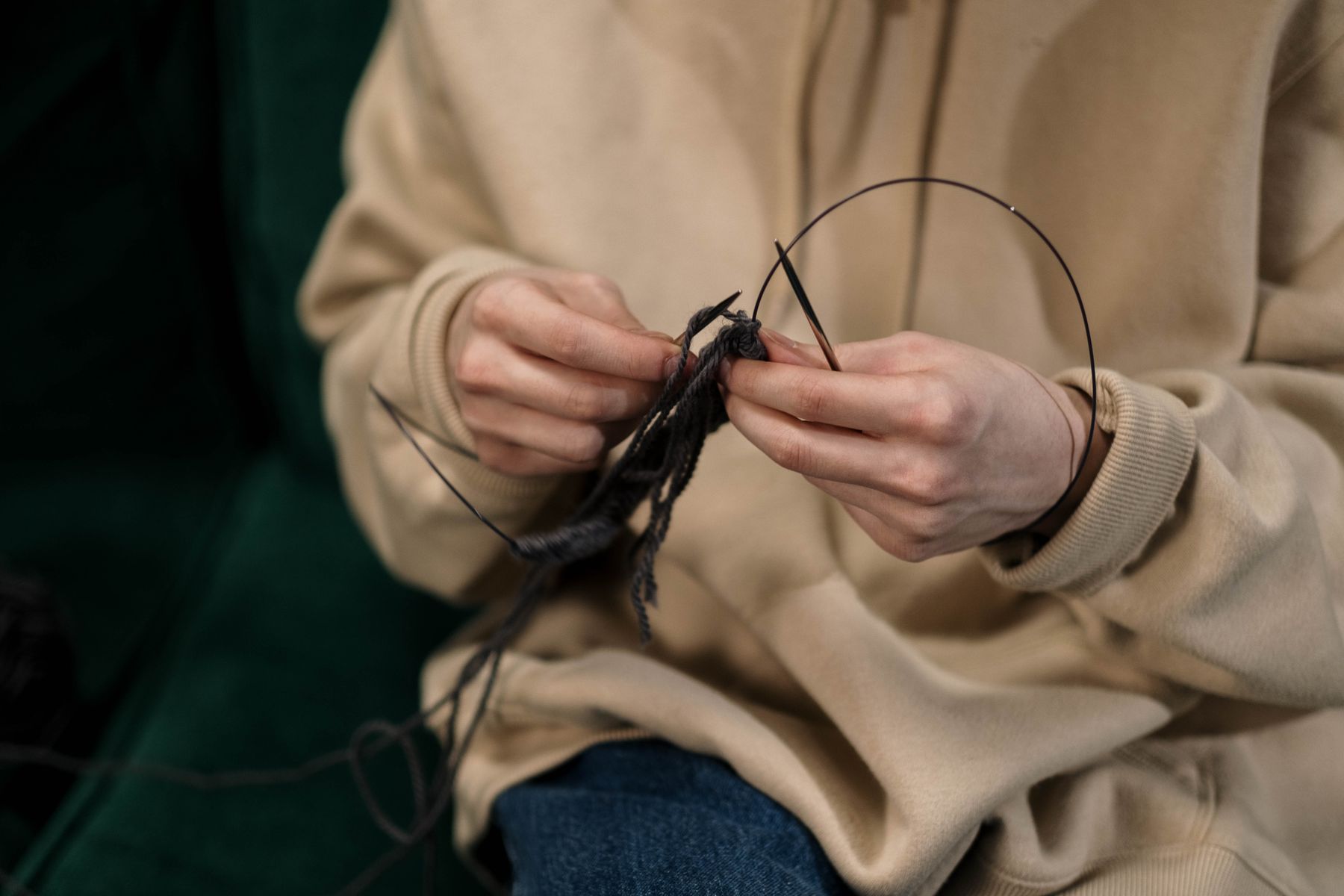 Hands knitting dark yarn with circular needles