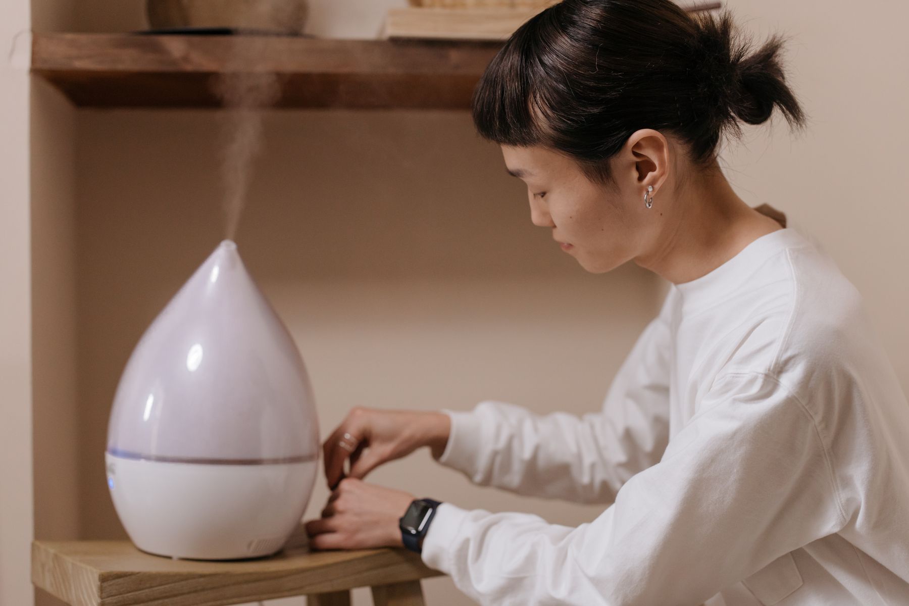 Person beside a white teardrop-shaped mist appliance on a table
