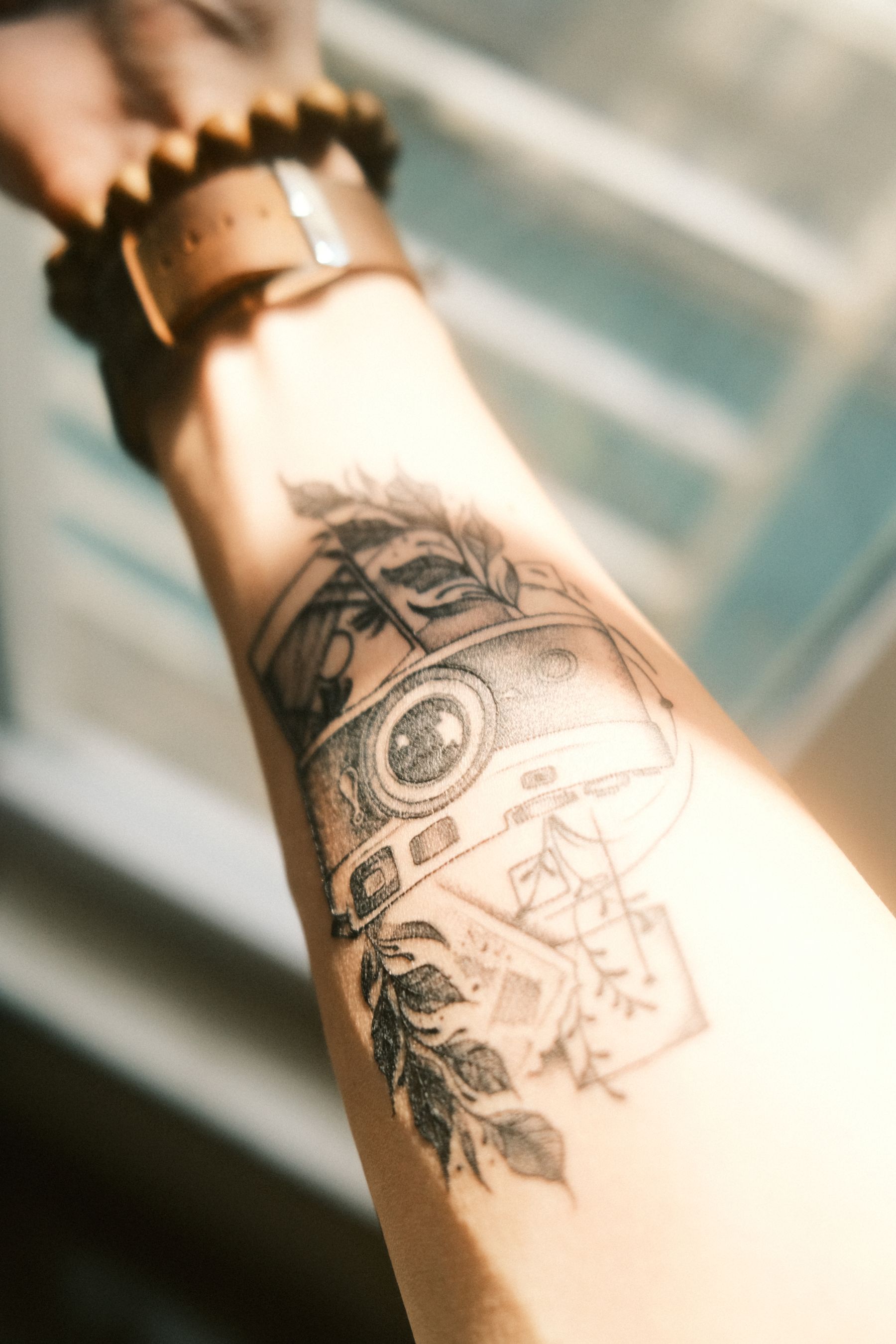 Camera-design tattoo on a forearm beside a wristwatch
