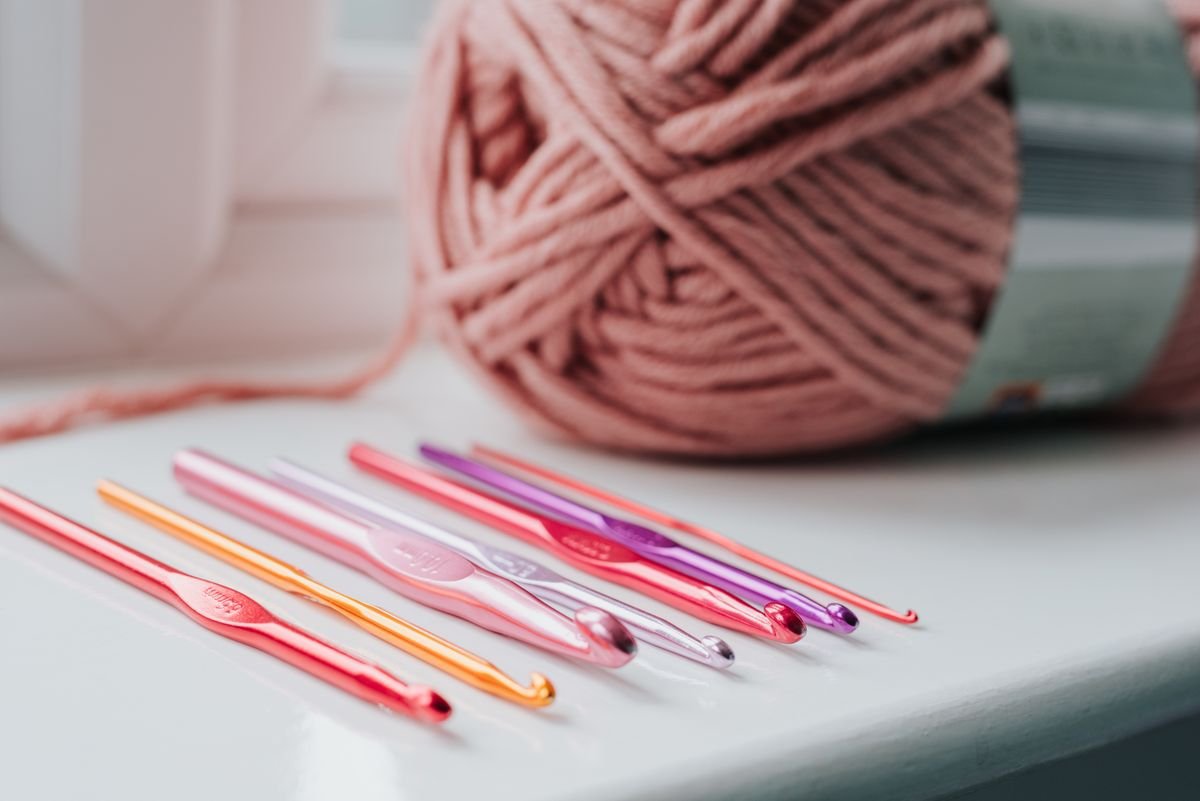 A set of crochet hooks with a ball of yarn on a bright windowsill.
