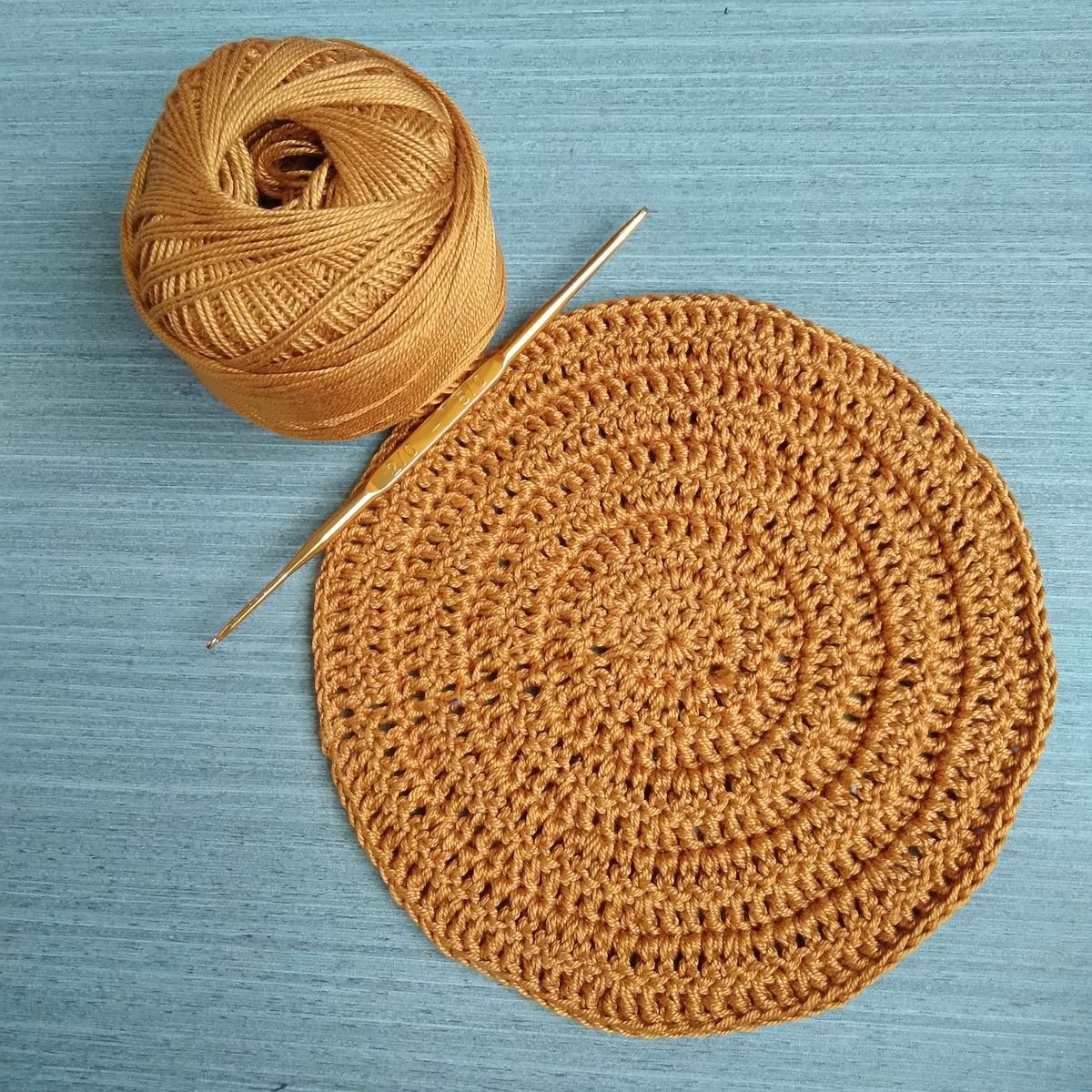 An orange crochet circle with a hook and yarn on a blue background.