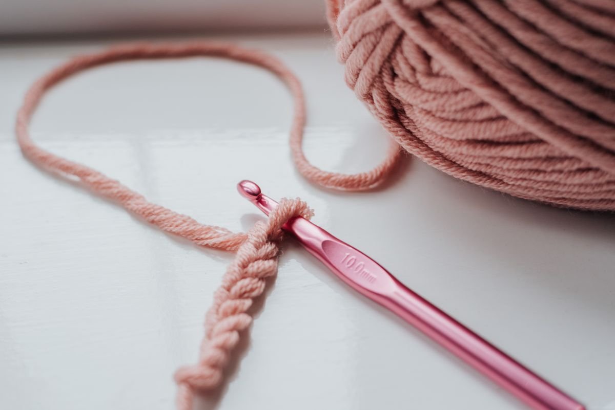 A narrow pink crochet work in progress with a hook and yarn.